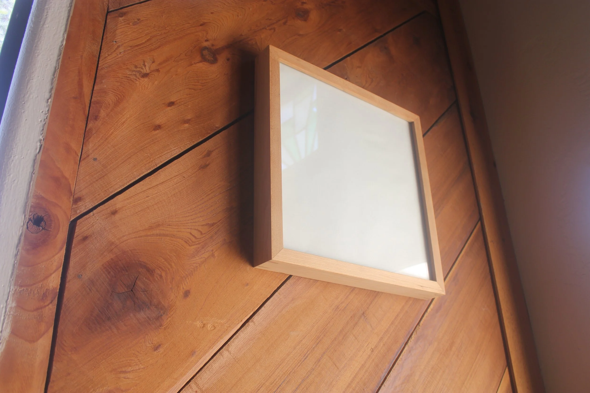 Gallery frame made of cherry shown against a wooden wall.