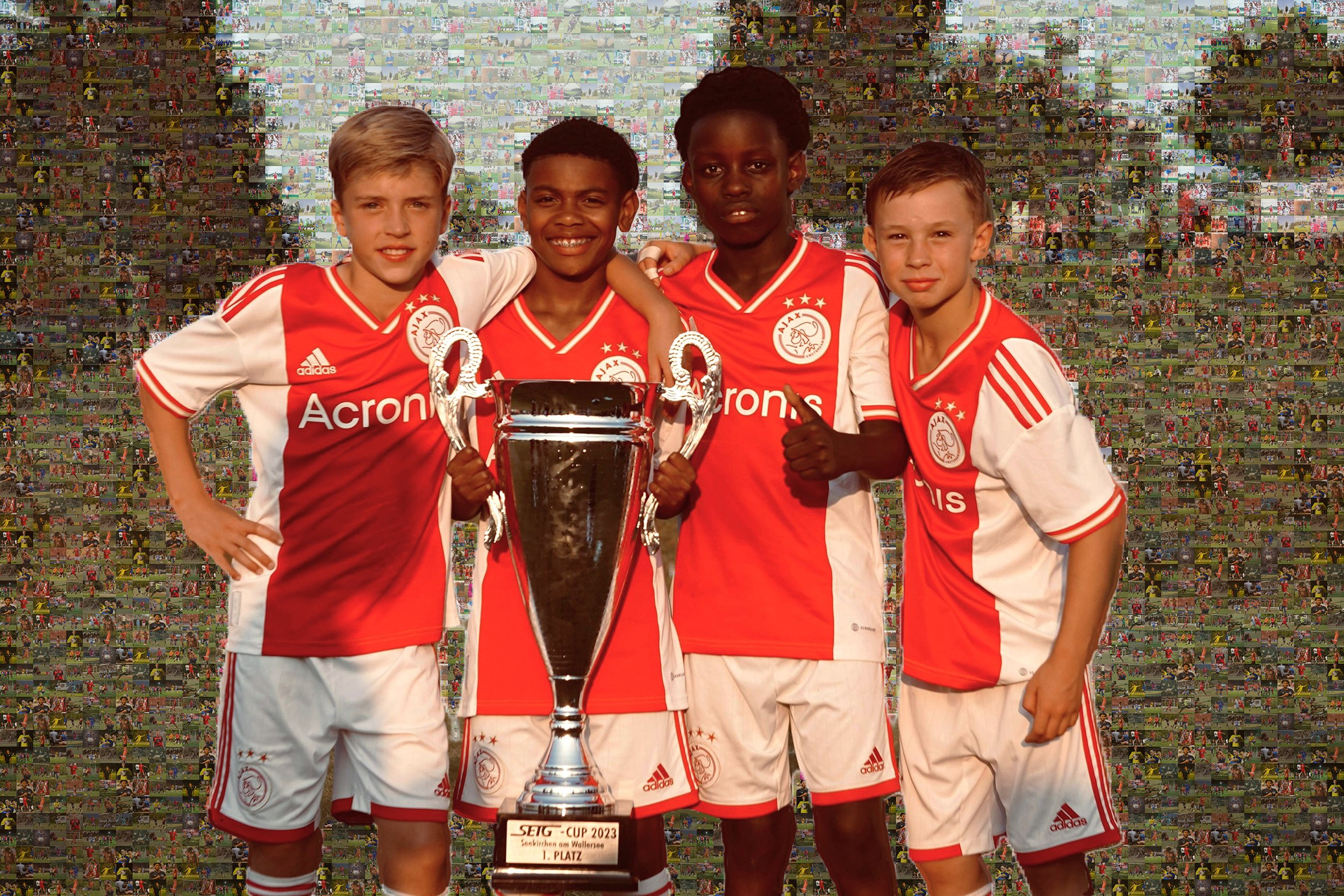 A group of four young happy male footballers pose in victory with a large silver trophy. They are wearing red jerseys with white sides and white shorts