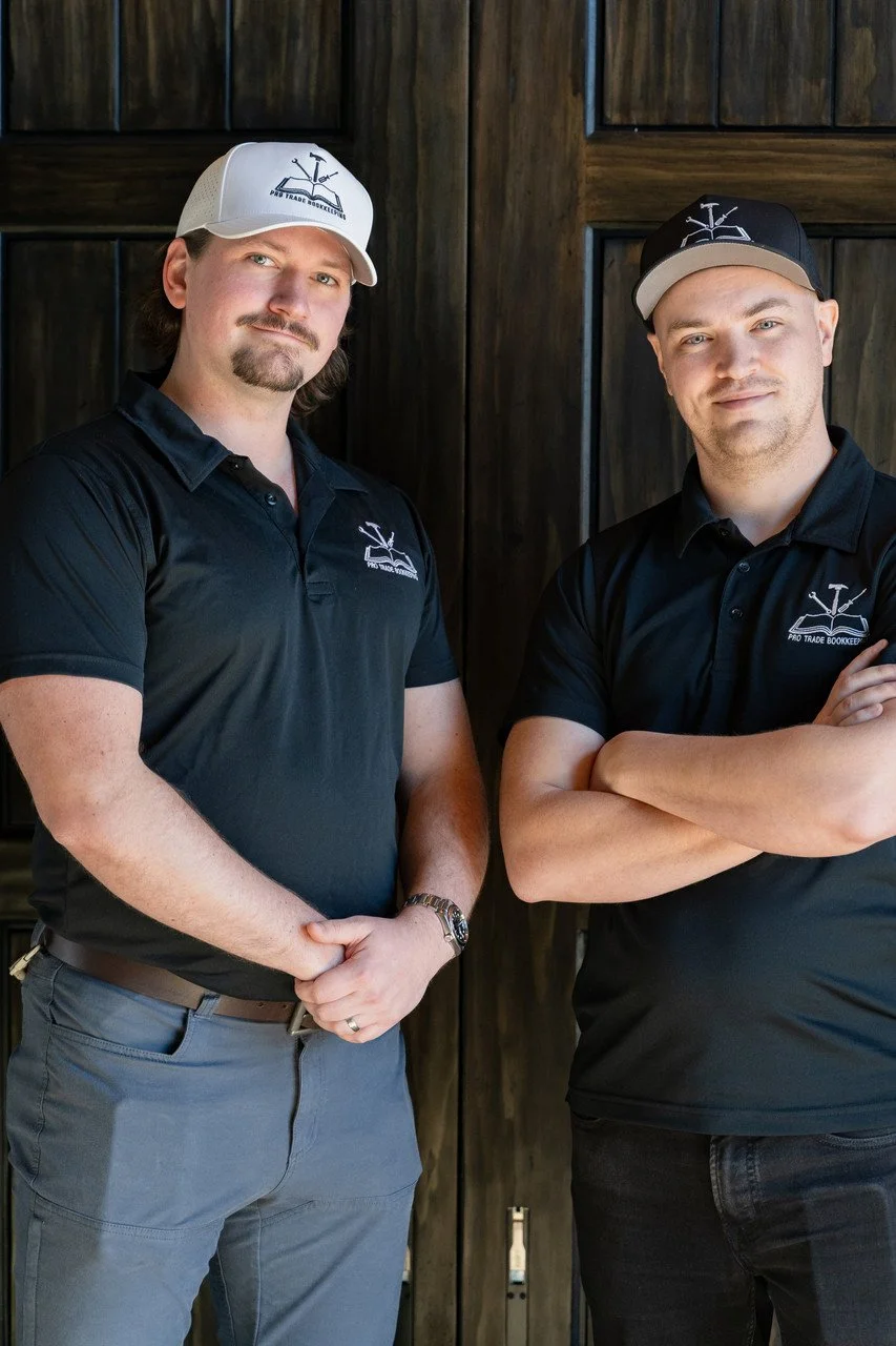Two men wearing black polo shirts and caps with logos standing in front of wooden panels.