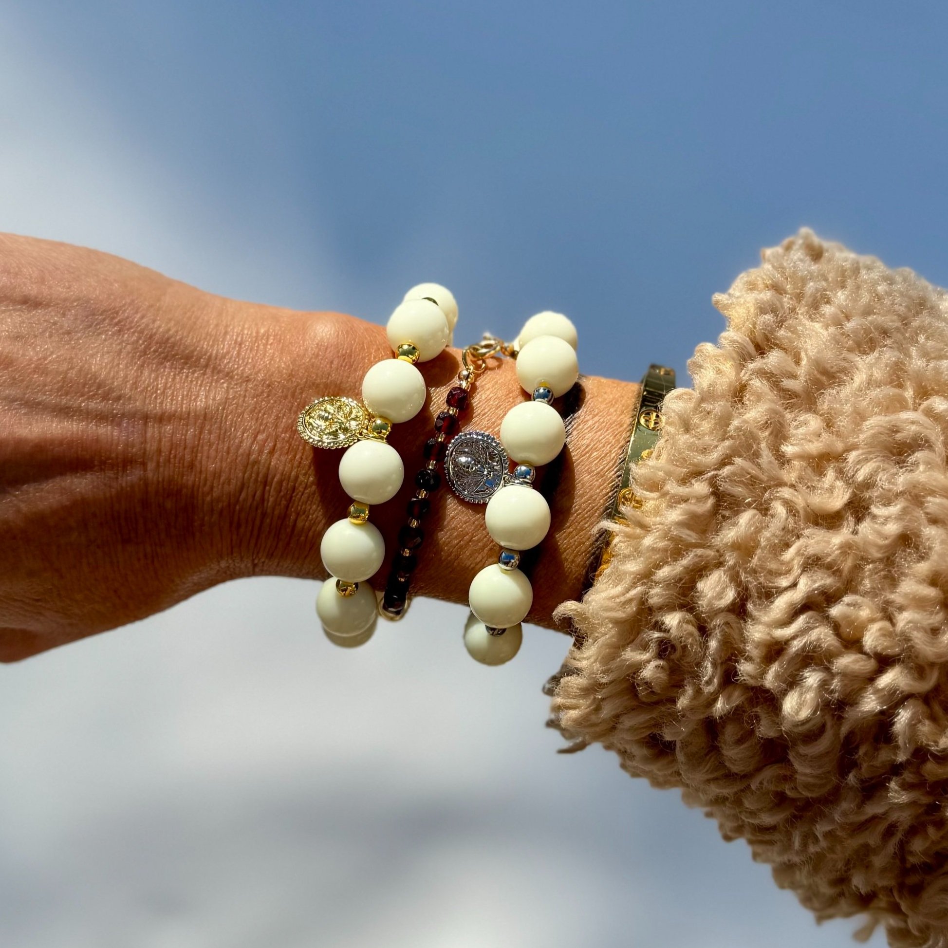 An ivory and gold charm bracelet and an ivory and silver charm bracelet shown on wrist.