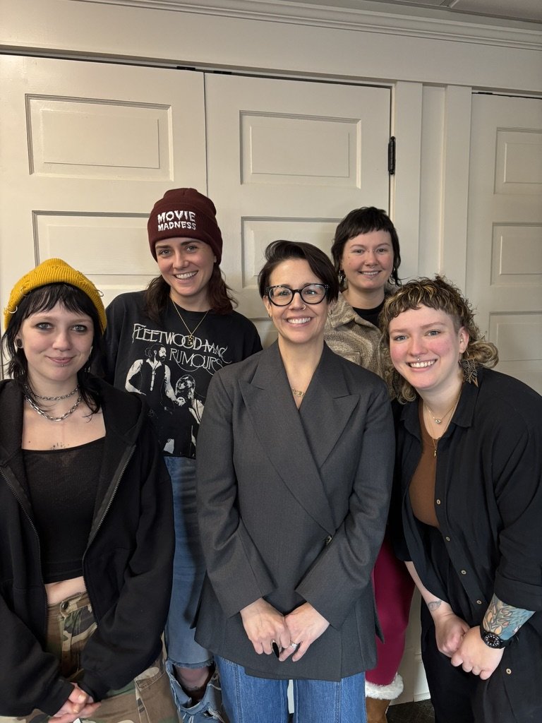 5 women stand in front of a white doorway, smiling at the camera after a workshop.