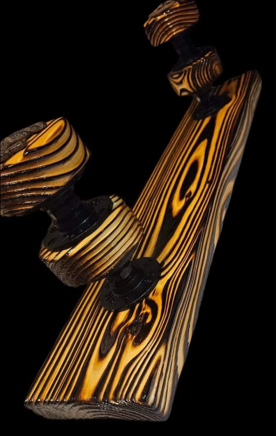 Close-up of a wooden skateboard with black wheels and trucks, focusing on the top deck and wheels against a black background.