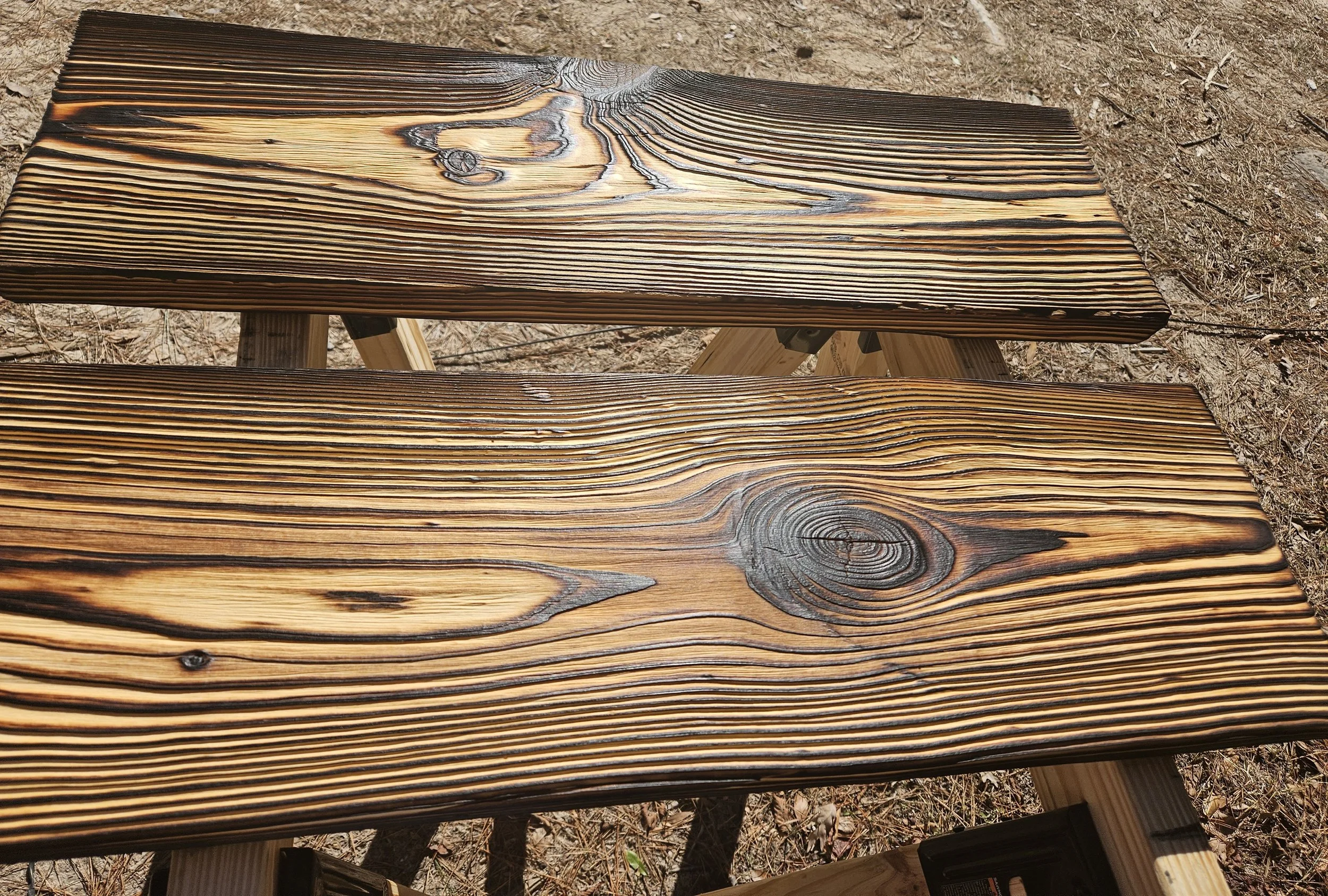 A wooden bench with visible wood grain, placed outdoors on dirt ground.