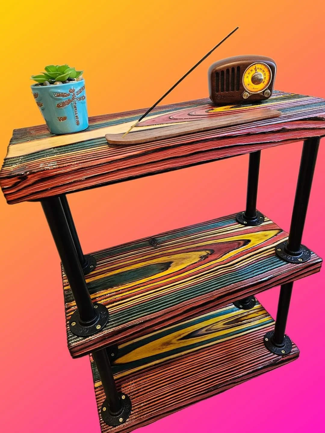 A colorful three-tiered wooden shelf with a small potted succulent plant, a wooden incense holder with a burning incense stick, and a vintage-style radio against an orange-pink gradient background.