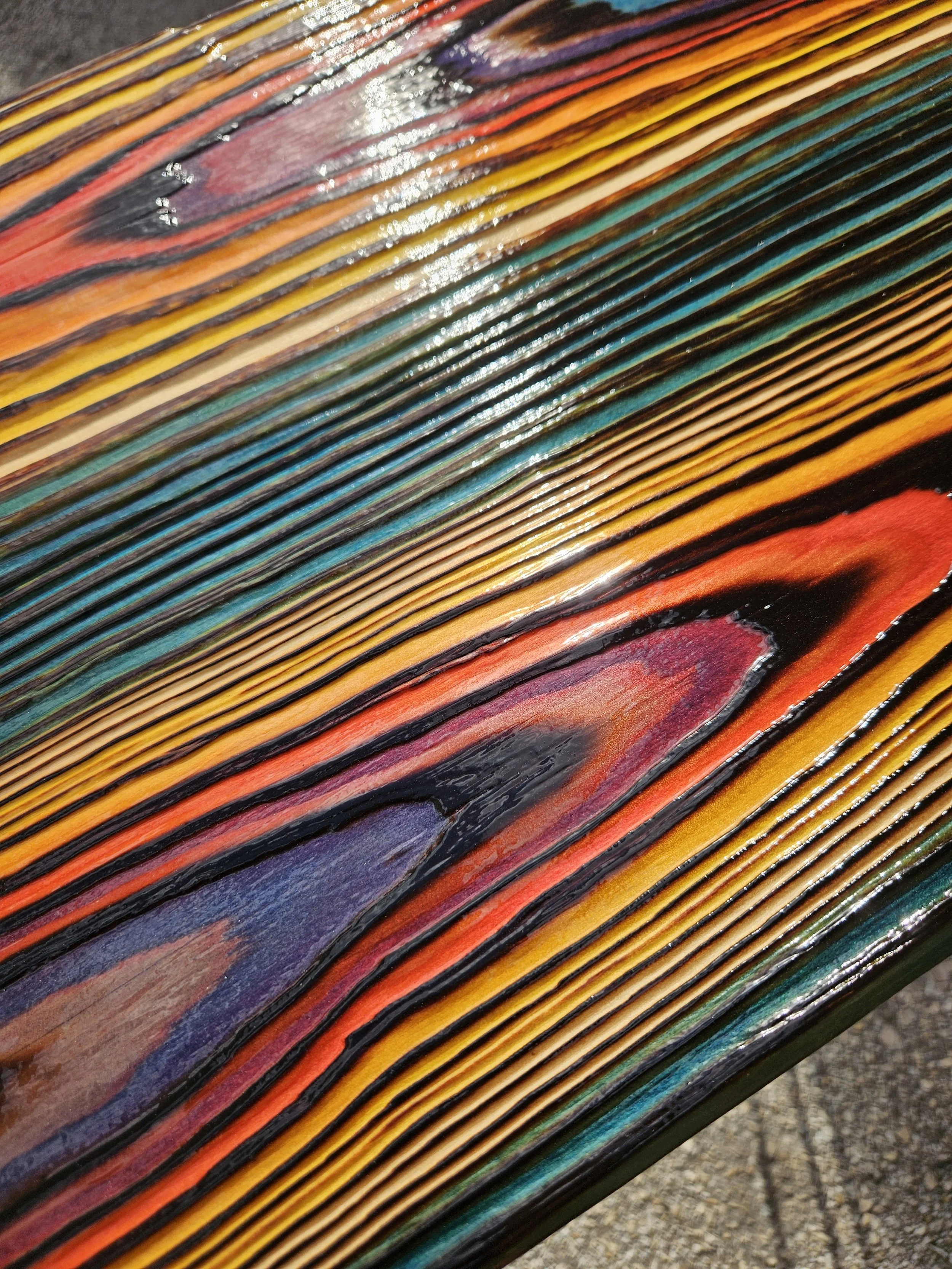 Close-up of a colorful feather with vibrant hues of yellow, orange, red, purple, teal, and black, showing detailed barbs and iridescent reflections.