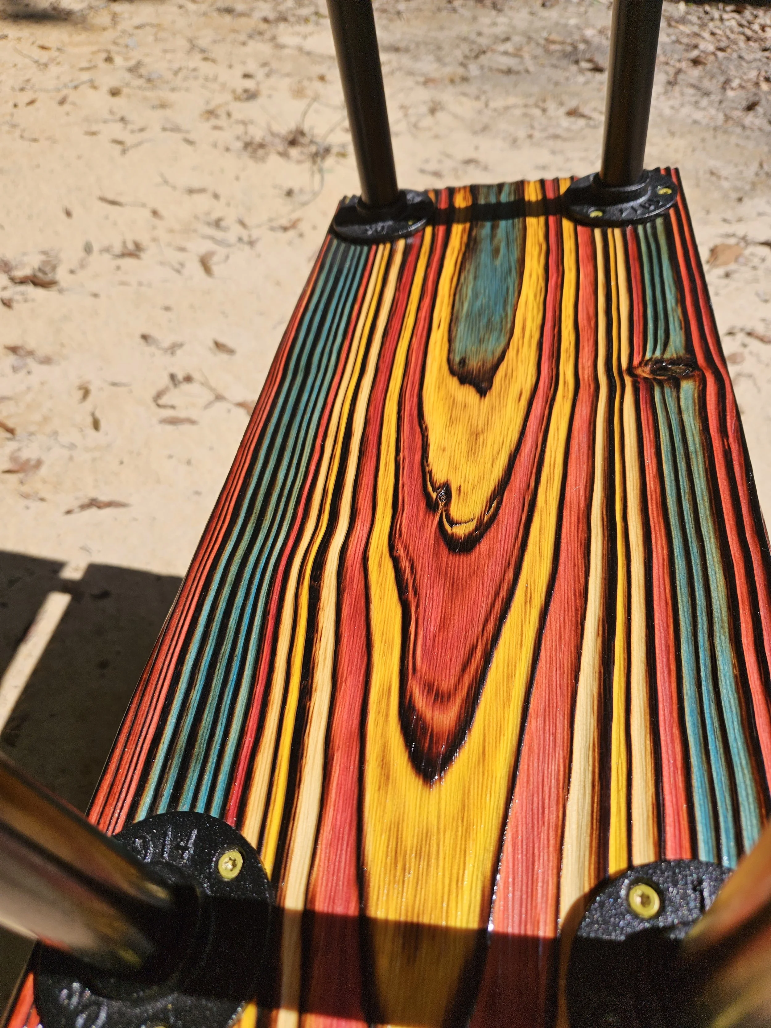 Close-up of a colorful wooden board, with black metal poles attached at the top and black metal base plates secured with yellow screws.