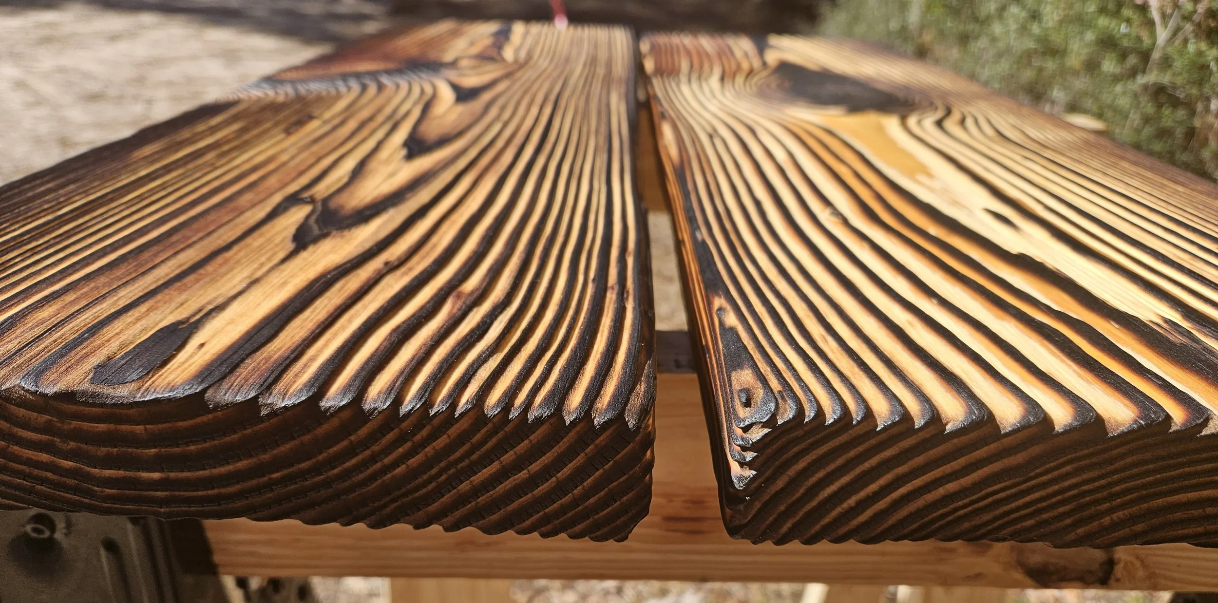 Close-up of a wooden outdoor table with burned-wood finish, highlighting the wood grain pattern.