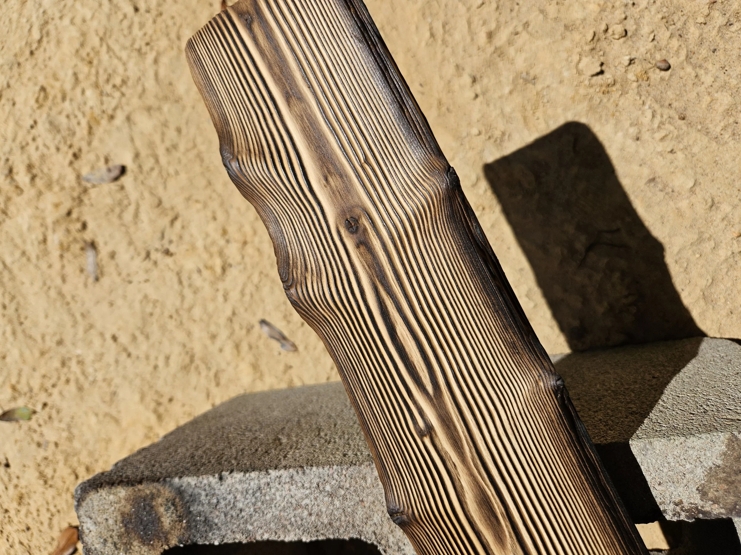 Close-up of a burnt wooden bench with visible wood grain on a sandy ground.