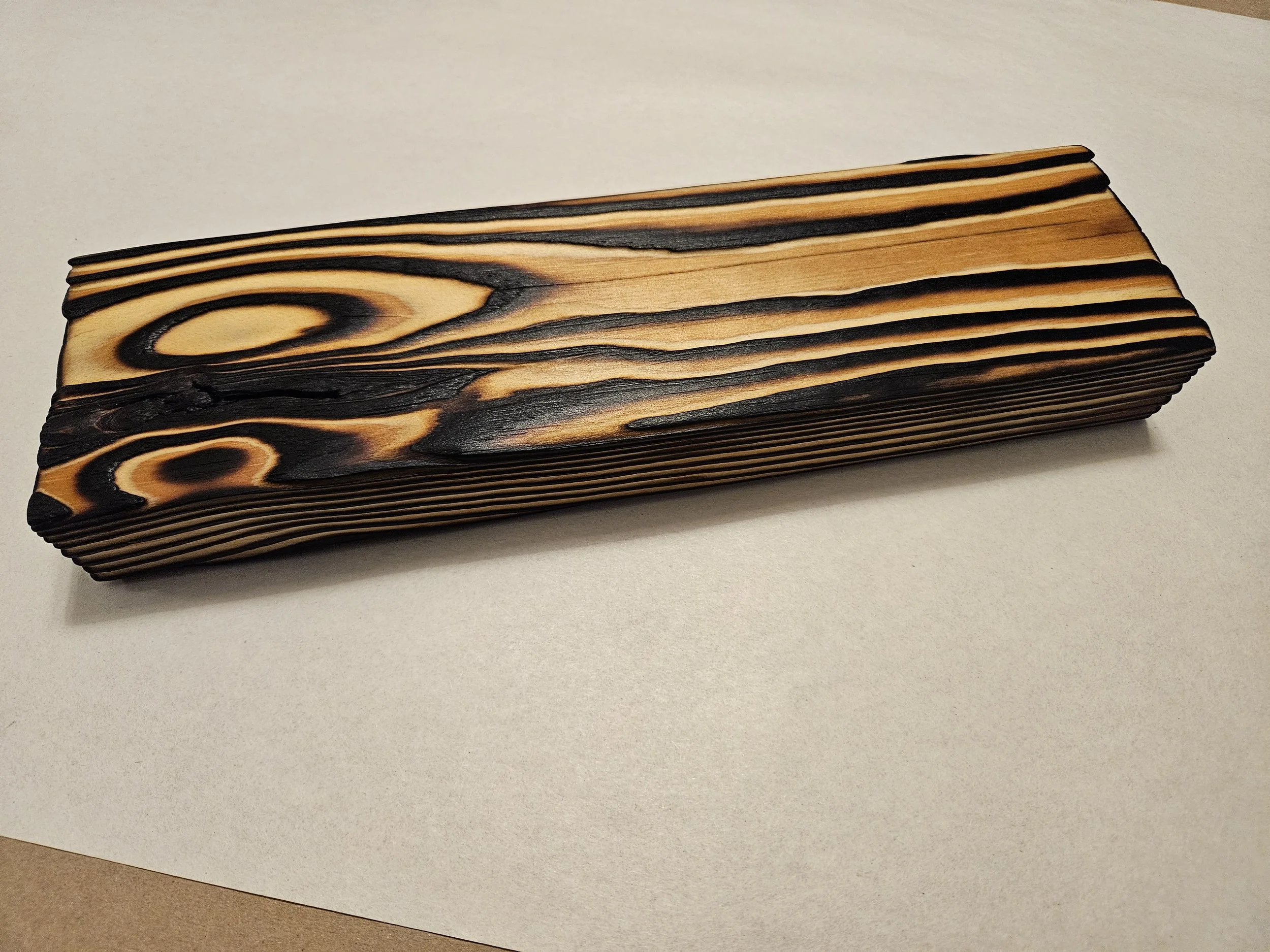 A piece of wood with burnt black patterns and lines resting on a white surface.