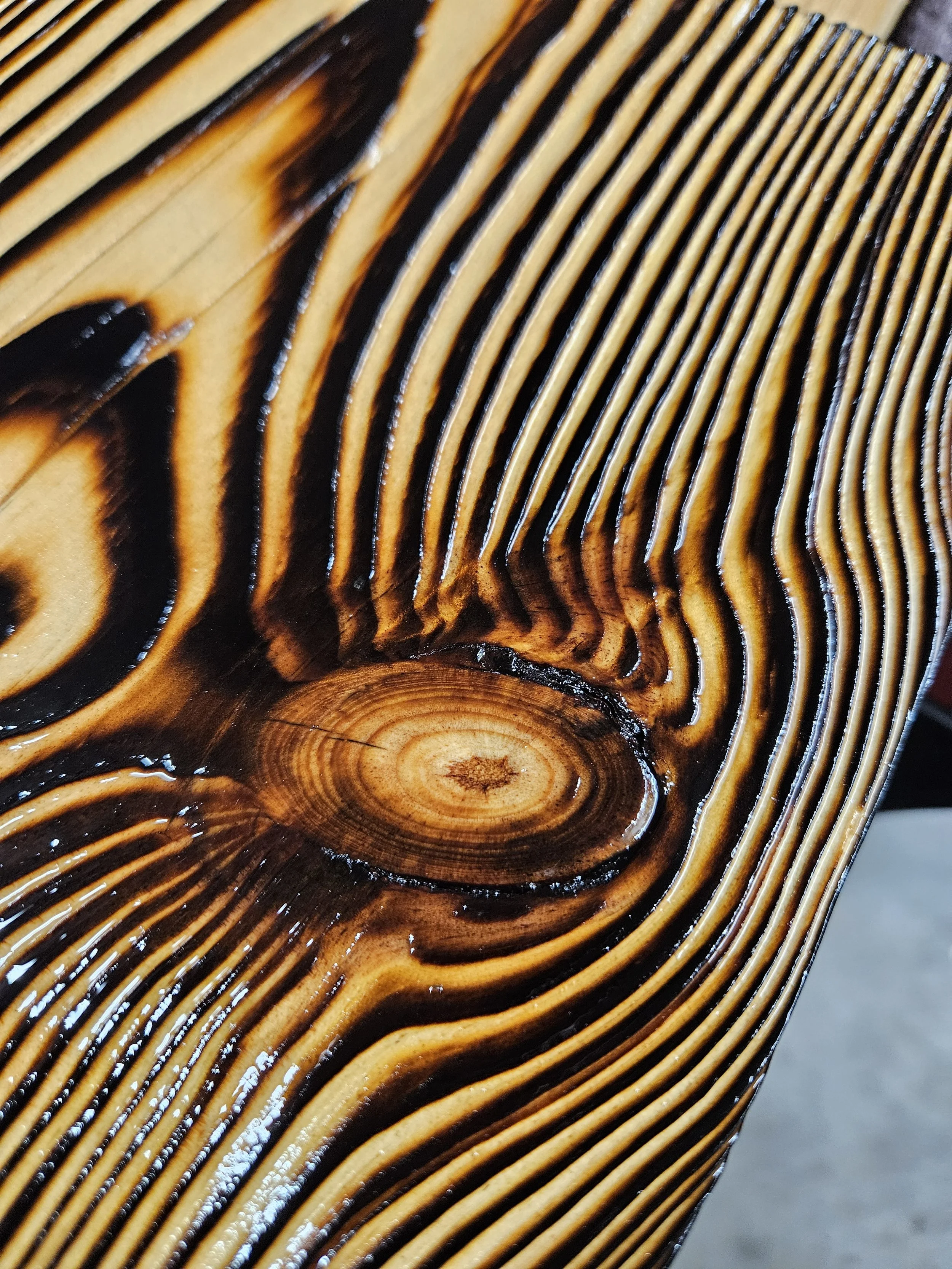 Close-up photograph of a wooden surface with dark and light brown grain patterns and concentric rings.