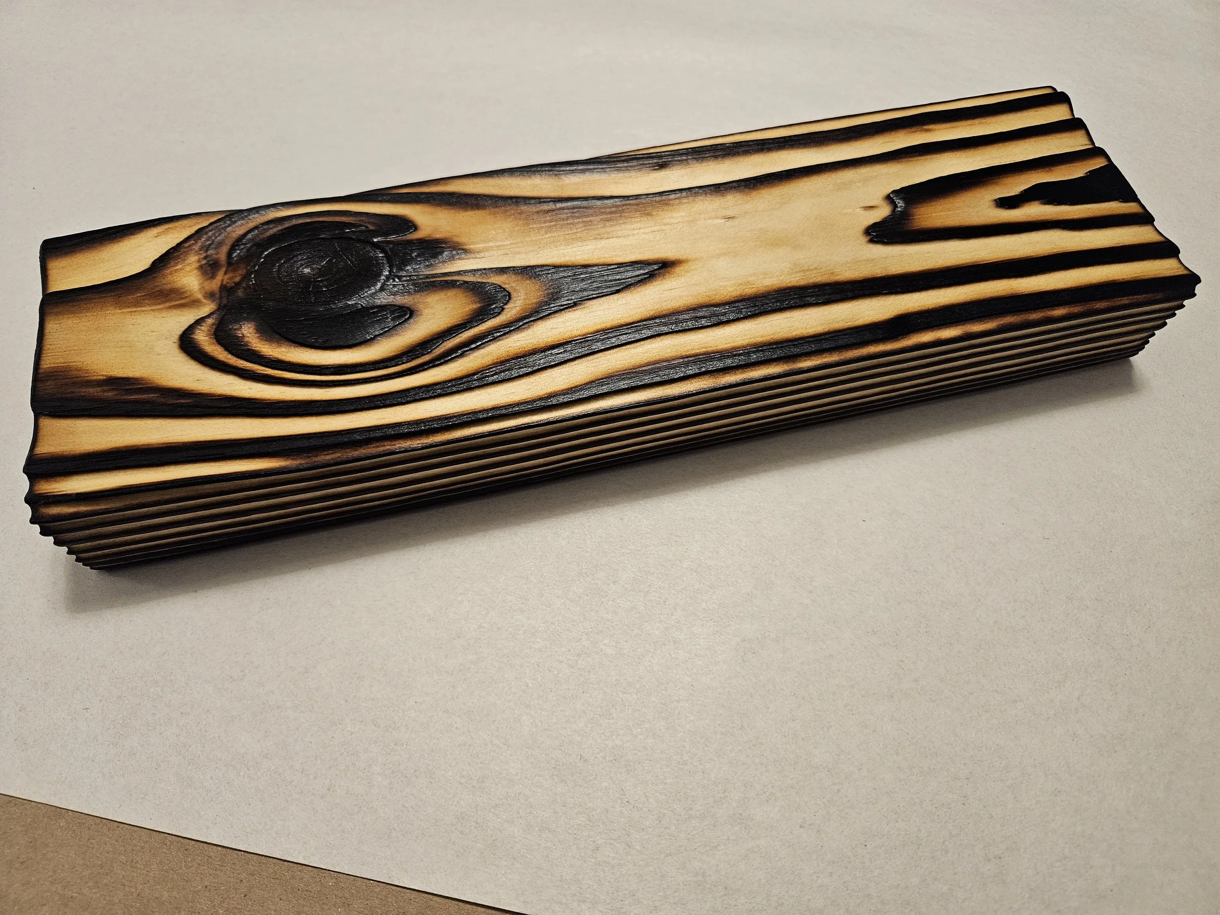 A piece of wood with visible grain patterns, featuring a large knot and darkened edges, resting on a white surface.