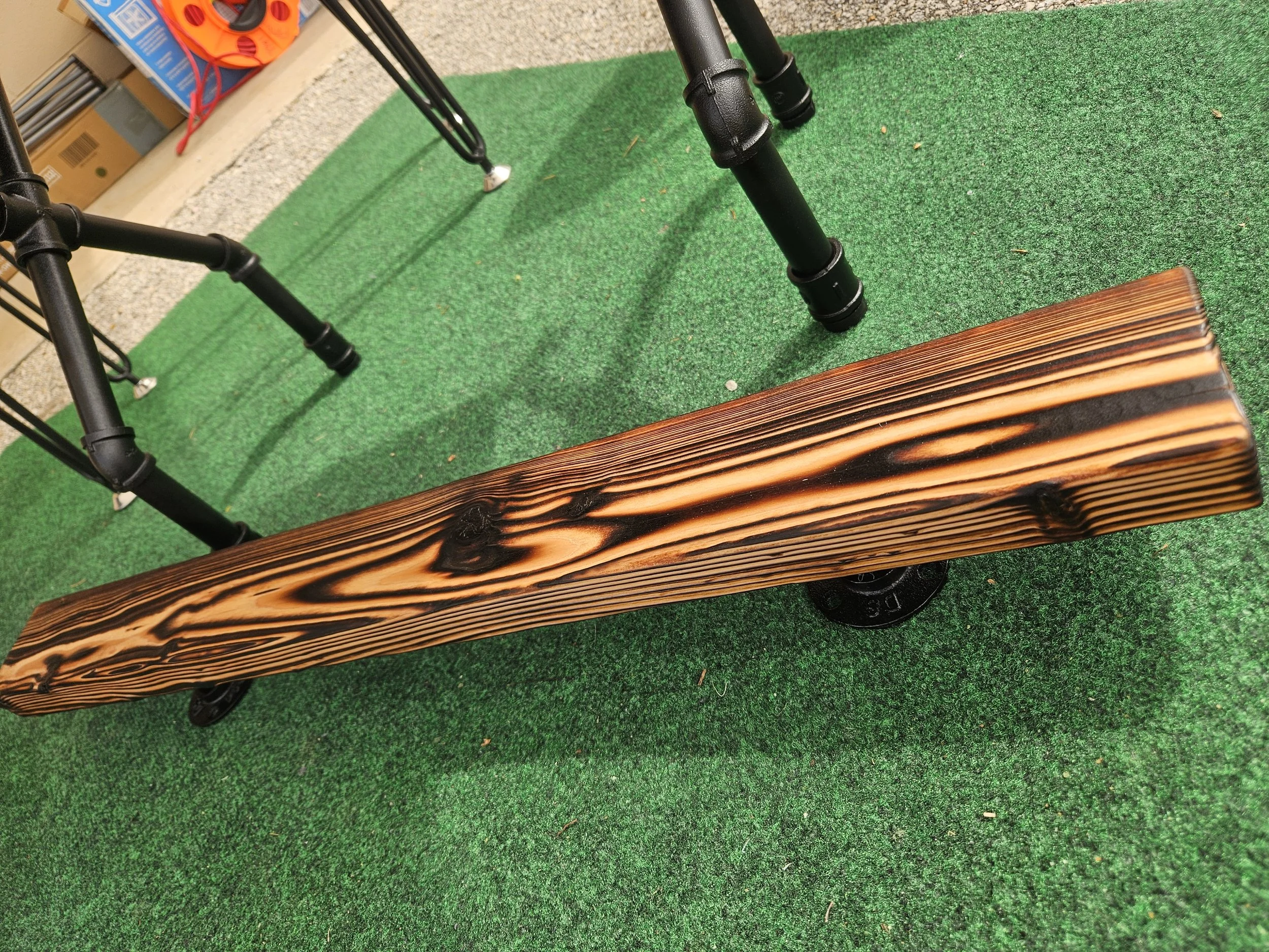 A black metal walking cane with a rubber tip on a green artificial grass surface, with a wooden bench at the edge and boxed items in the background.
