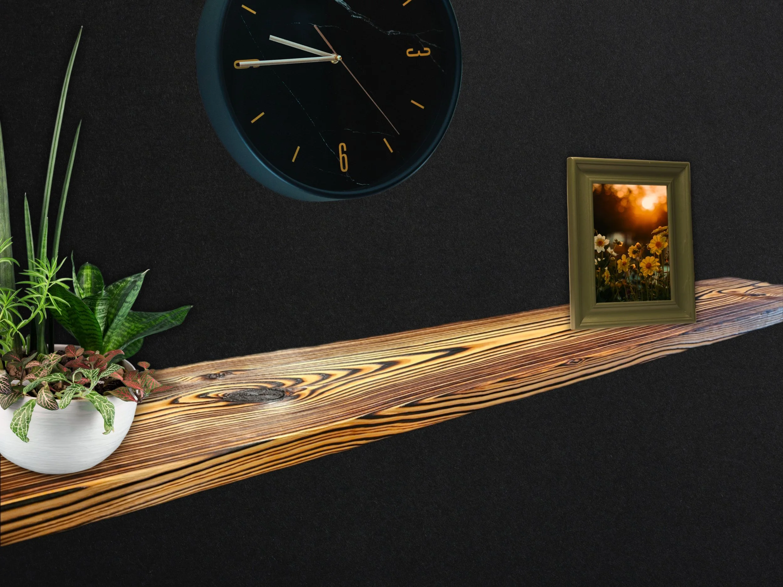 Close-up of a black clock with gold numbers and white hands, showing approximately 12:13. A green framed photo with a sunset scene and flowers is next to the clock. The items are on a wooden surface against a black background.