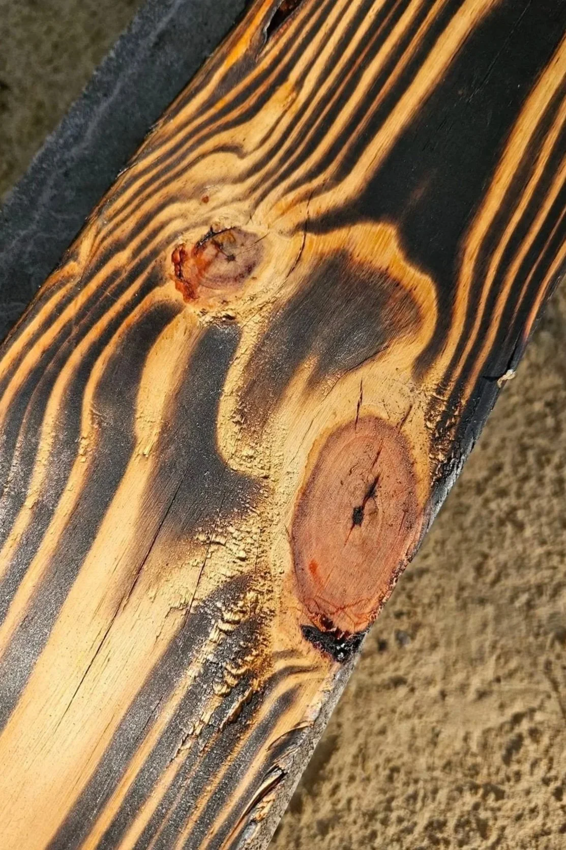 Close-up of fire-darkened wood showing knots, color variation, and raised grain.