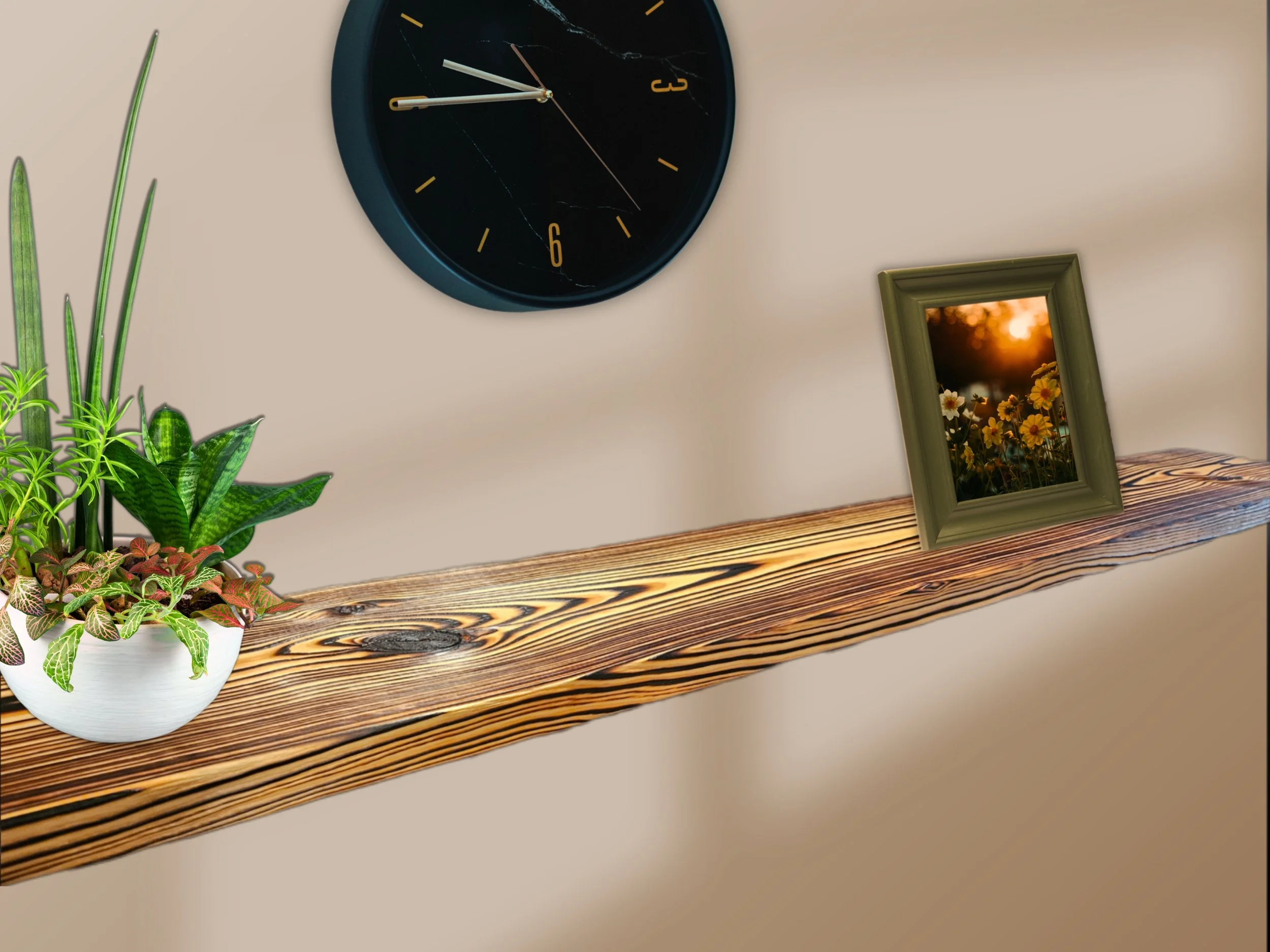 A black clock with gold numbers and hands, plants in a white pot, a framed sunset photo, and a wooden shelf.