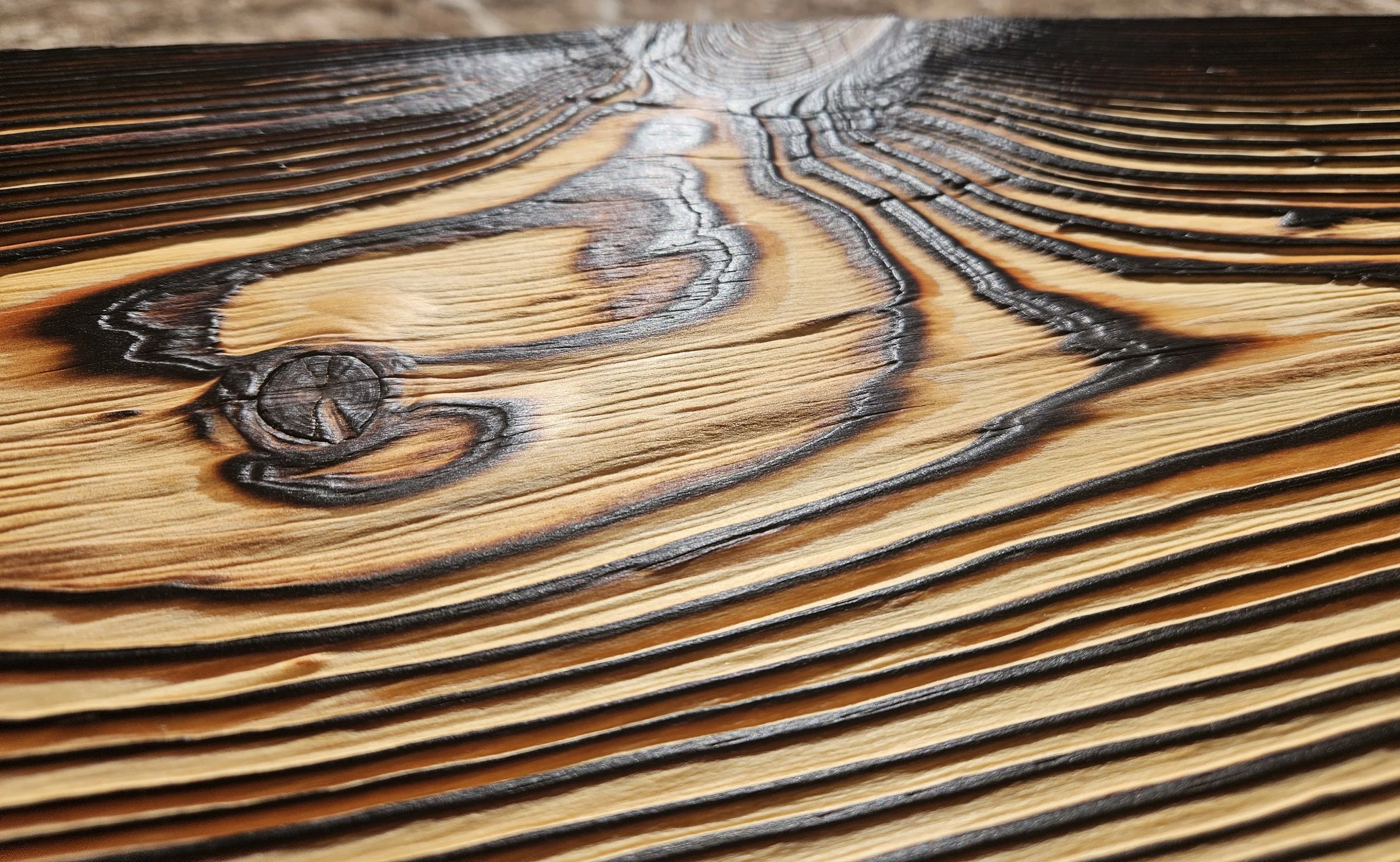 Close-up of a wooden surface with burnt and charred markings highlighting wood grain and knots.