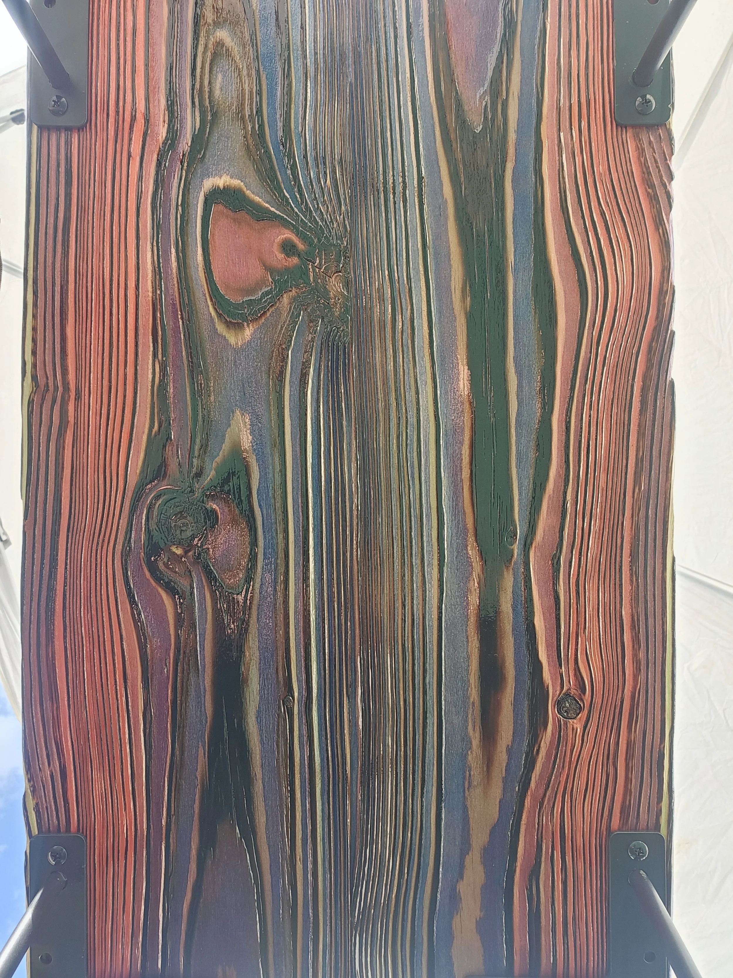 Close-up of a colorful wooden surface with a swirling grain pattern, mounted on a black frame with visible screws.
