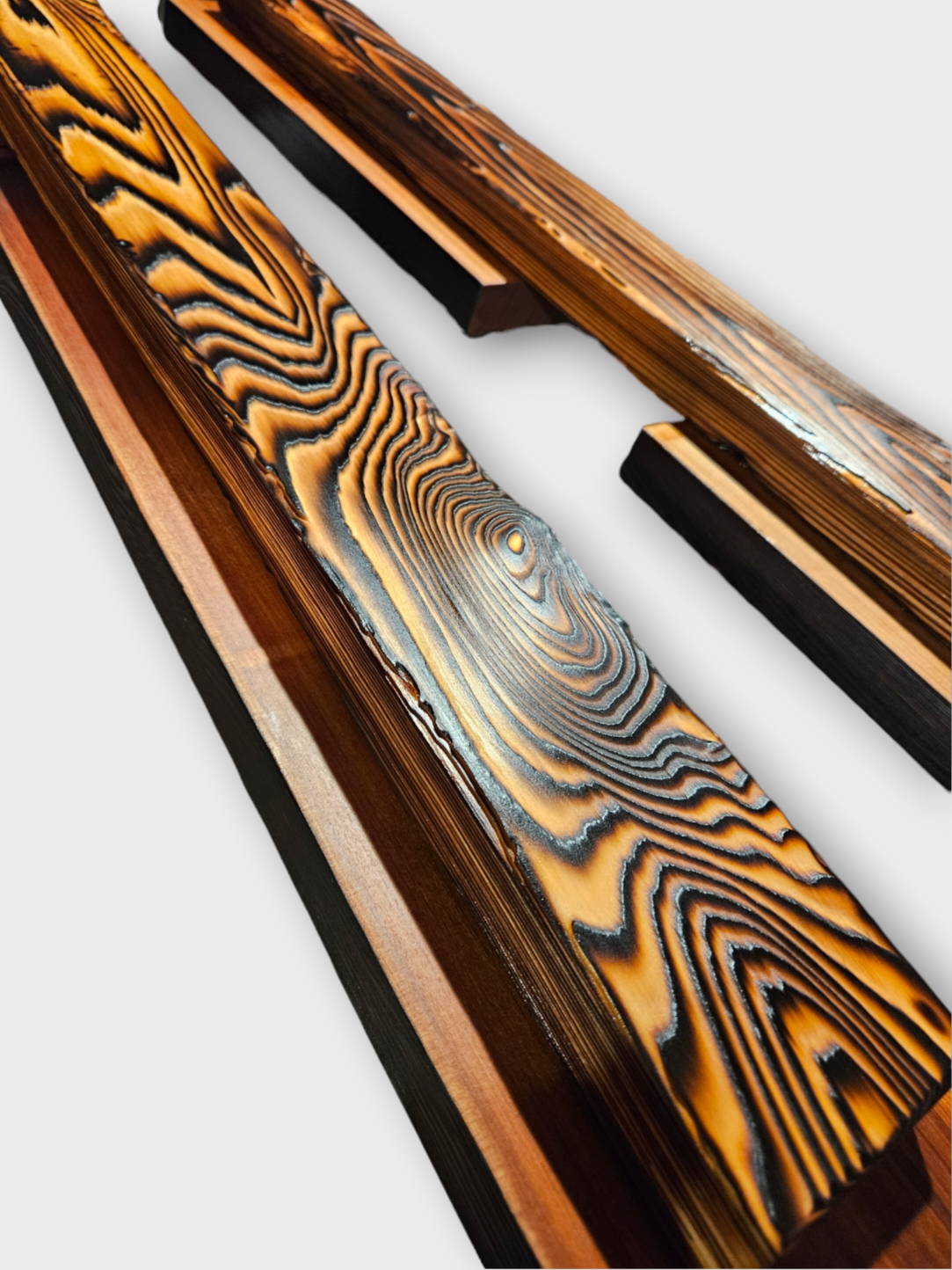 Close-up of two pieces of burned wood with charred and patterned surfaces against a white background.