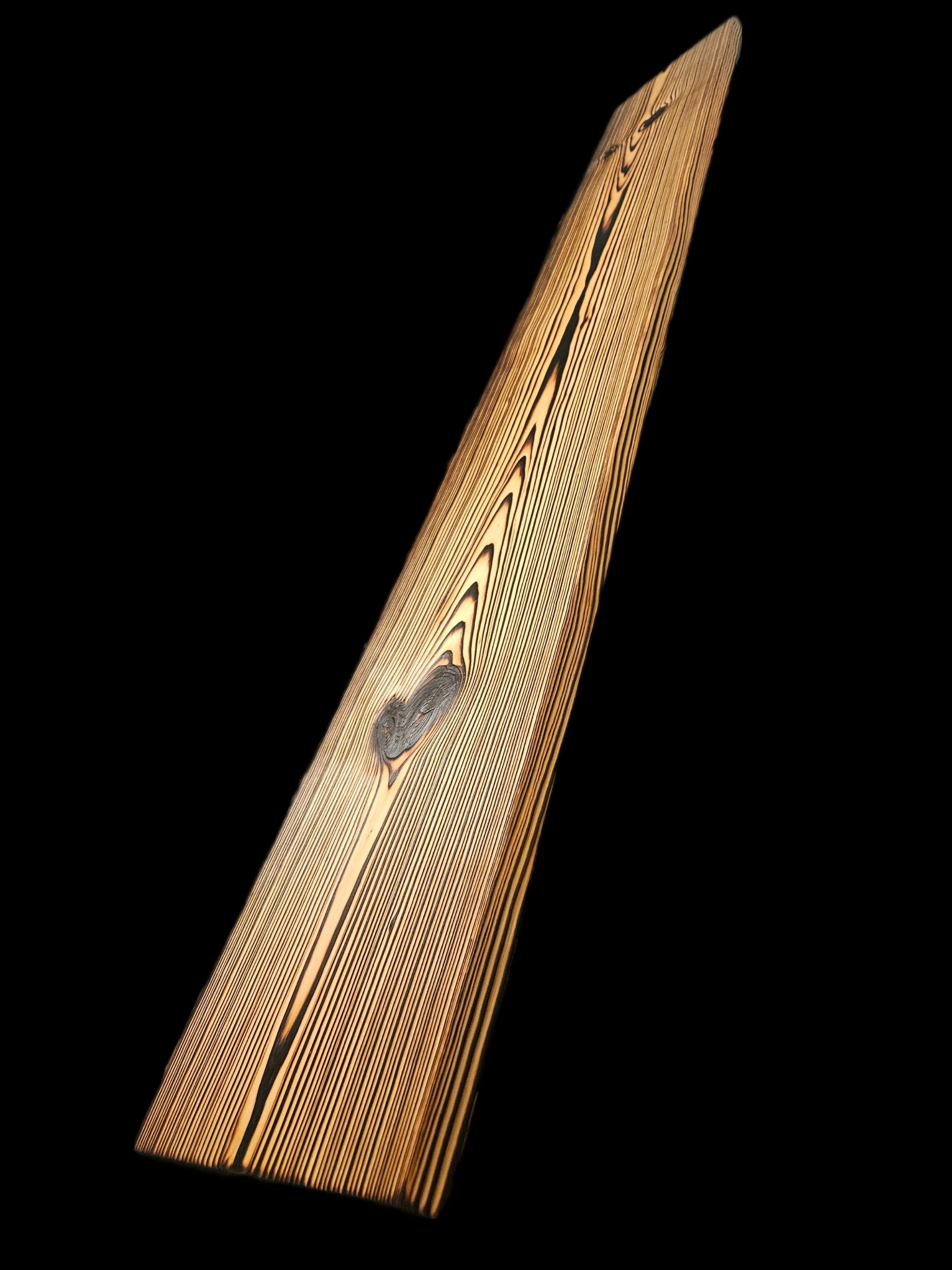 A close-up image of a wooden board with visible grain and knots, set against a black background.