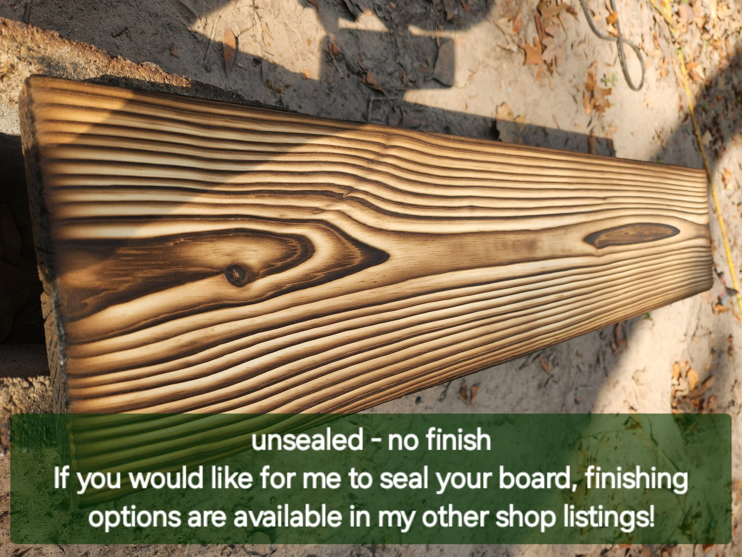 A close-up of a wood board with a natural, textured grain pattern, resting on a concrete surface outdoors with fallen leaves around. There is an overlayed green text section at the bottom with white text: "unsealed - no finish" and part of a longer m