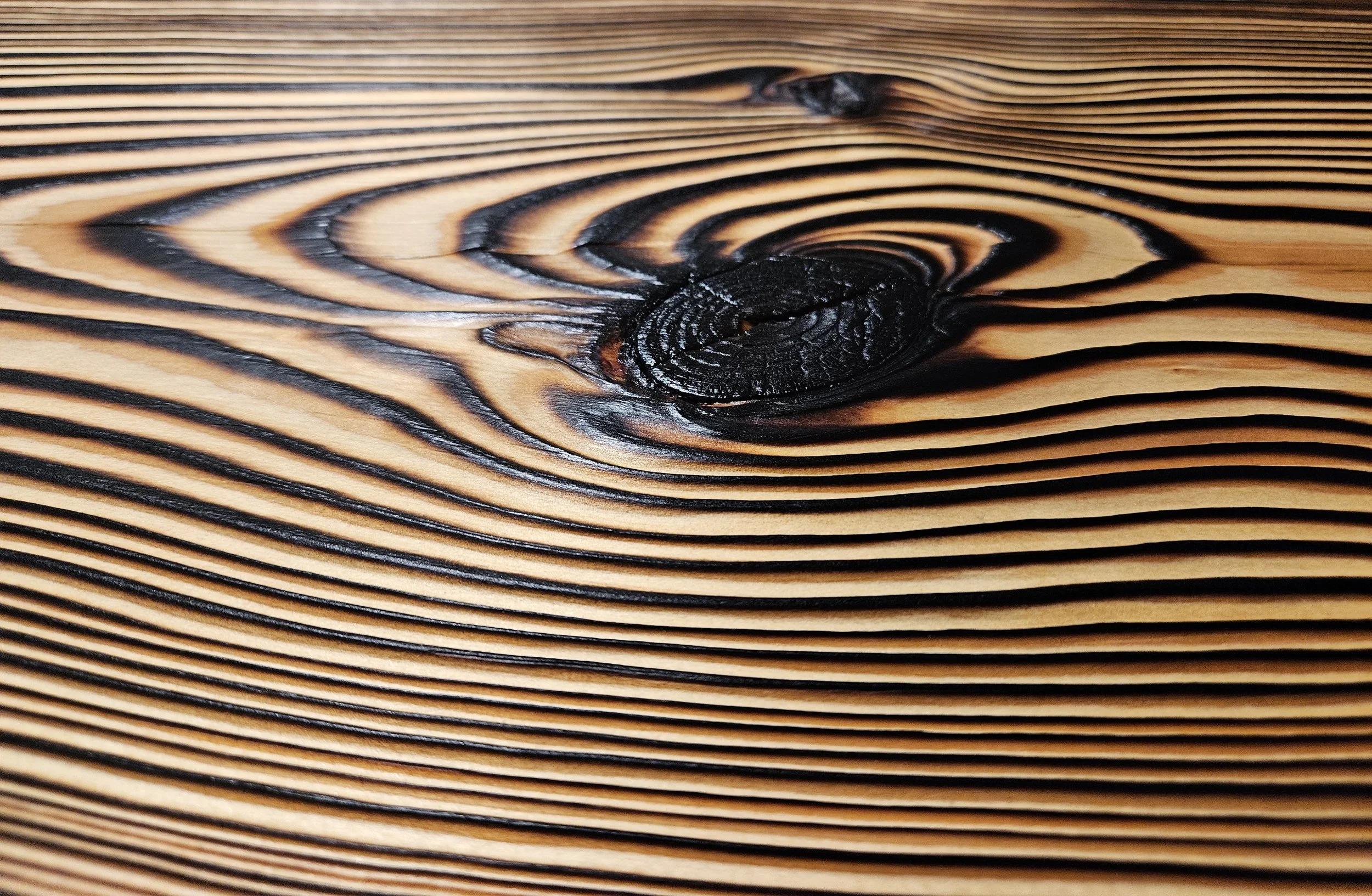 Close-up of a wooden surface with parallel dark and light wood grain lines and a prominent knot near the center.
