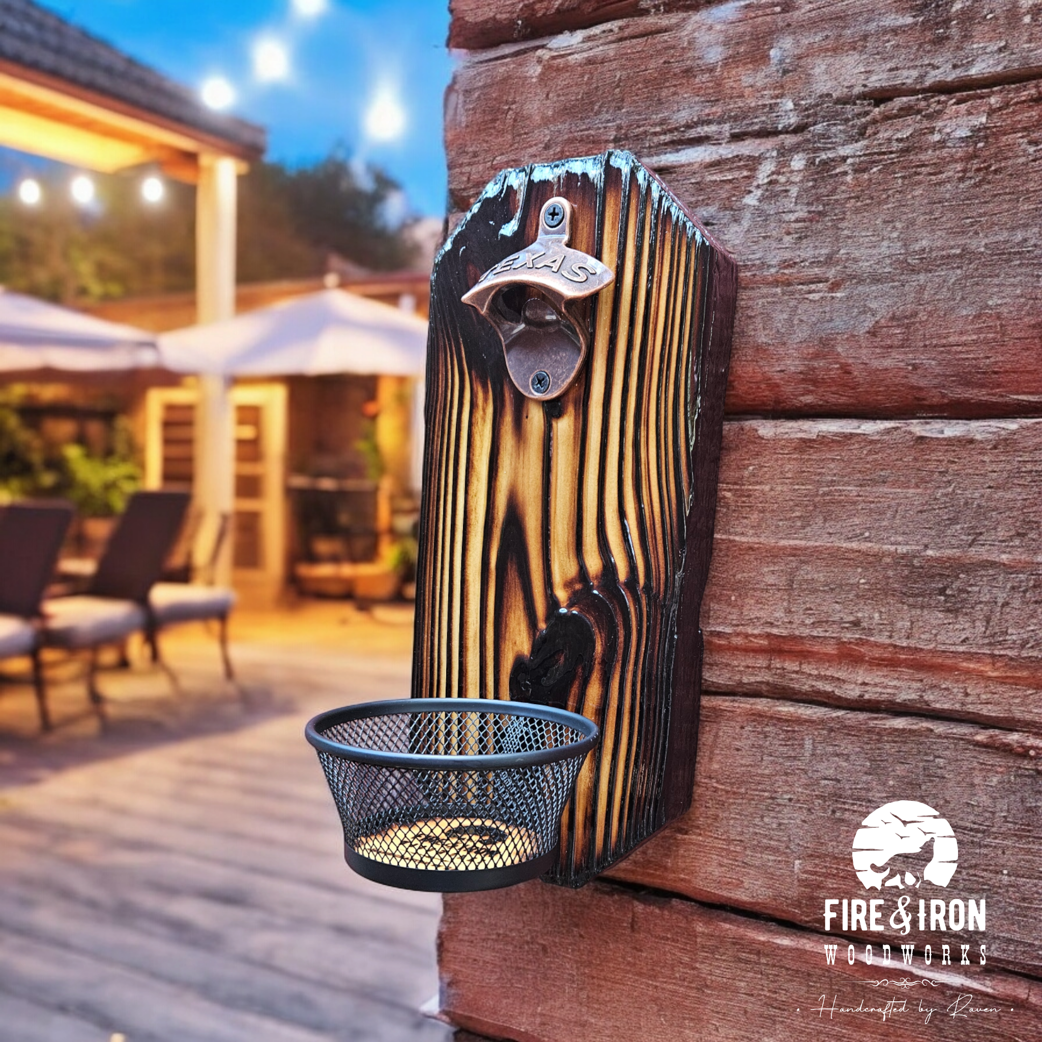 Close-up of a wooden post with a metal fire alarm latch labeled 'TEXAS' mounted on it. Surrounding the post are wooden slats and a metal trash bin with a rounded, hole pattern at the bottom. In the background, there is outdoor furniture, a patio umbr