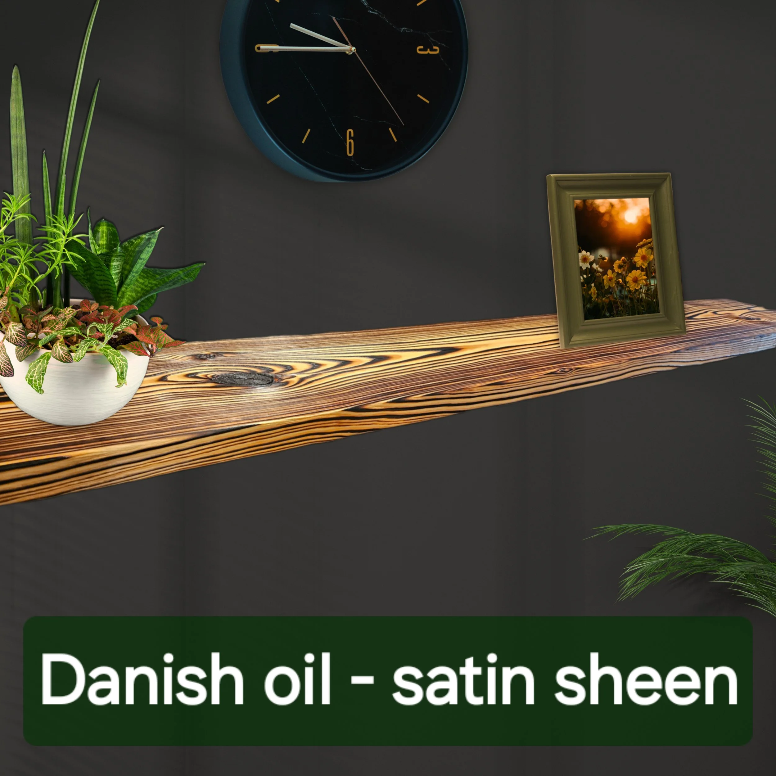 A black wall clock with gold numbers and white hands showing the time as 11:55. A framed photograph of flowers at sunset and a white pot with green and purple plants are on a wooden surface below the clock.