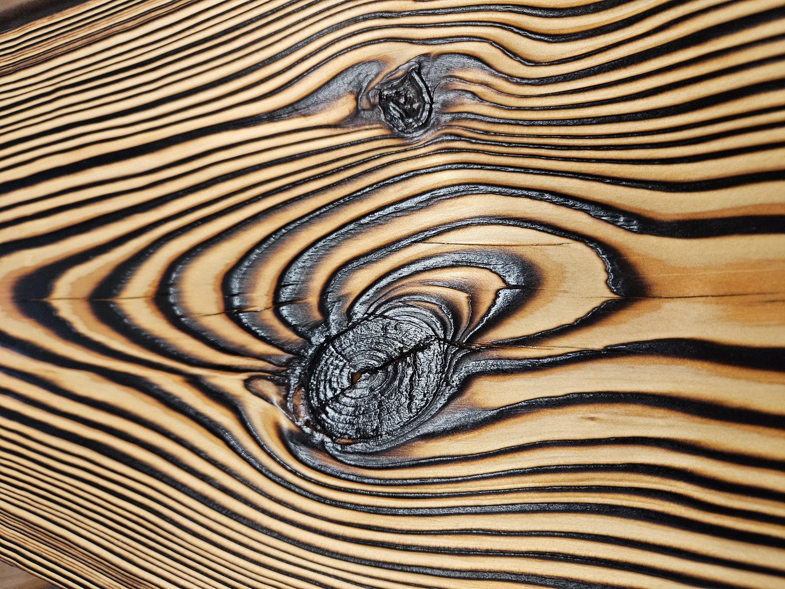 Close-up of a piece of wood with a prominent dark knot in the center and light and dark grain lines radiating outward.