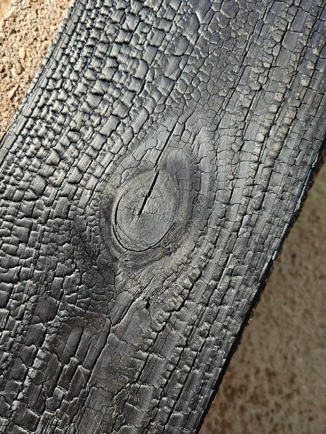 Close-up of a dark FireForged™ wood surface showing pronounced grain and a natural knot.