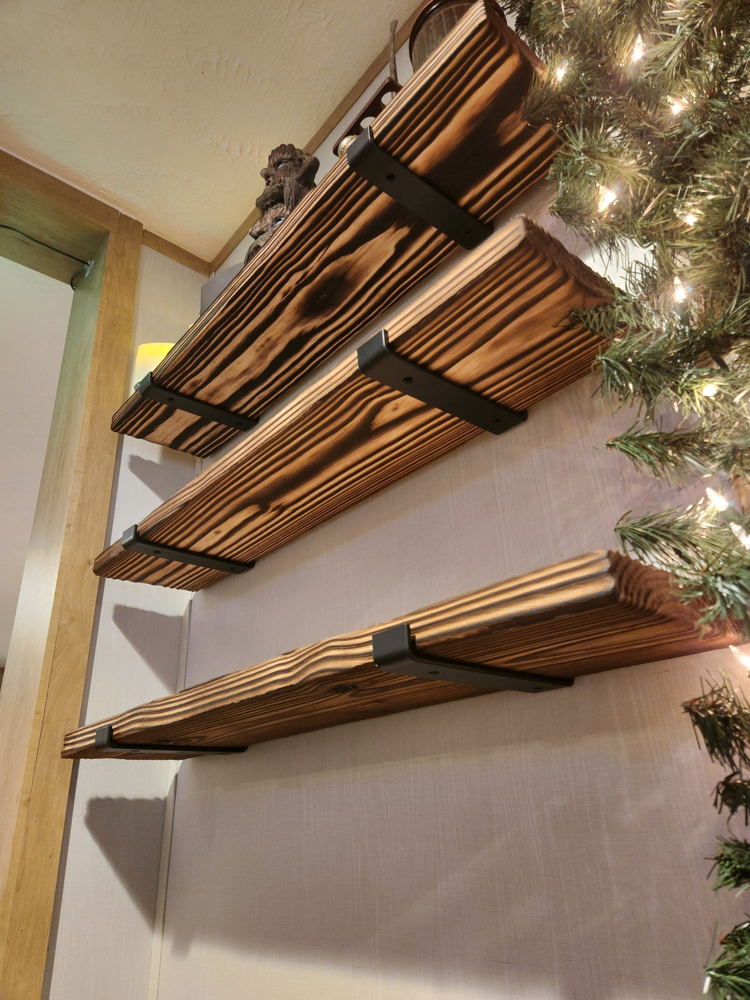 Wooden shelves with black brackets mounted on a wall surrounded by holiday greenery and lights.