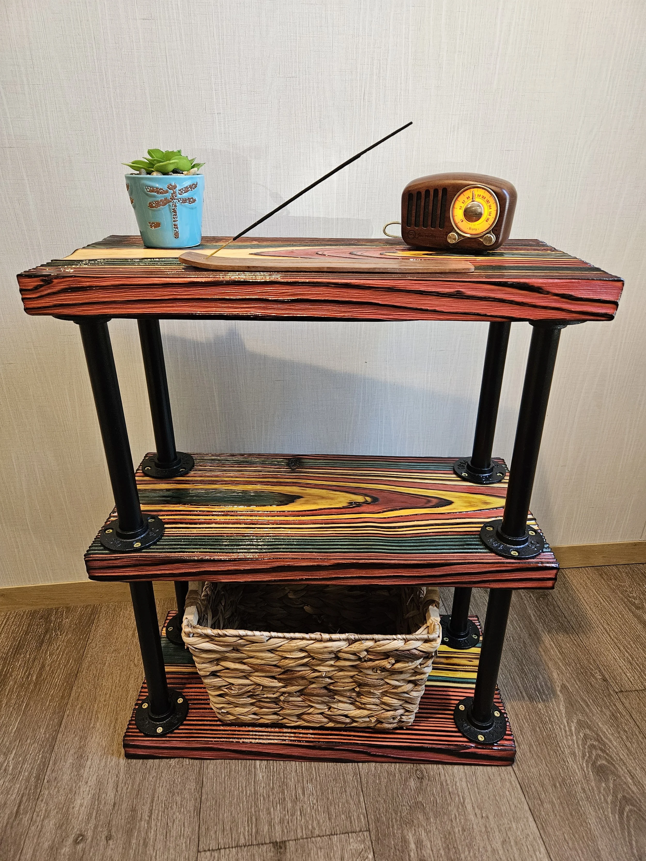 A wooden table with a small potted succulent plant, an old-fashioned radio, a decorative incense holder, and a woven basket underneath.