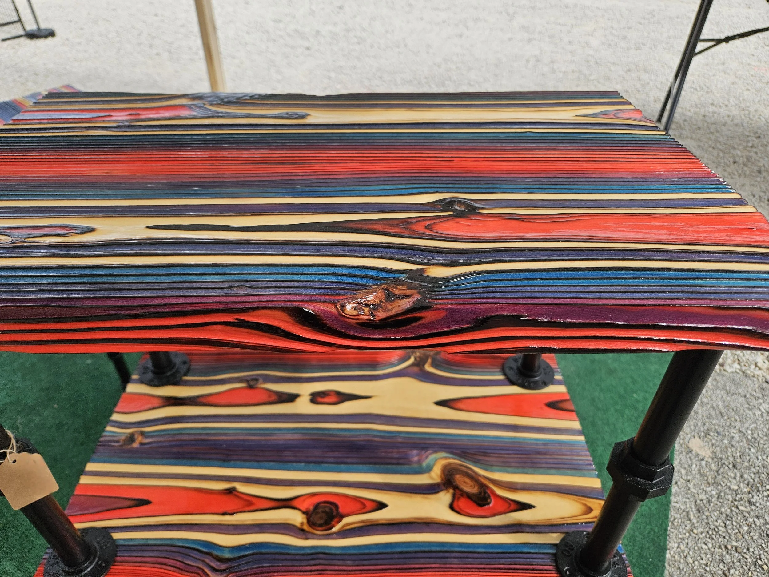 Colorful wooden benches with a black metal frame on a patch of artificial green turf and gravel.
