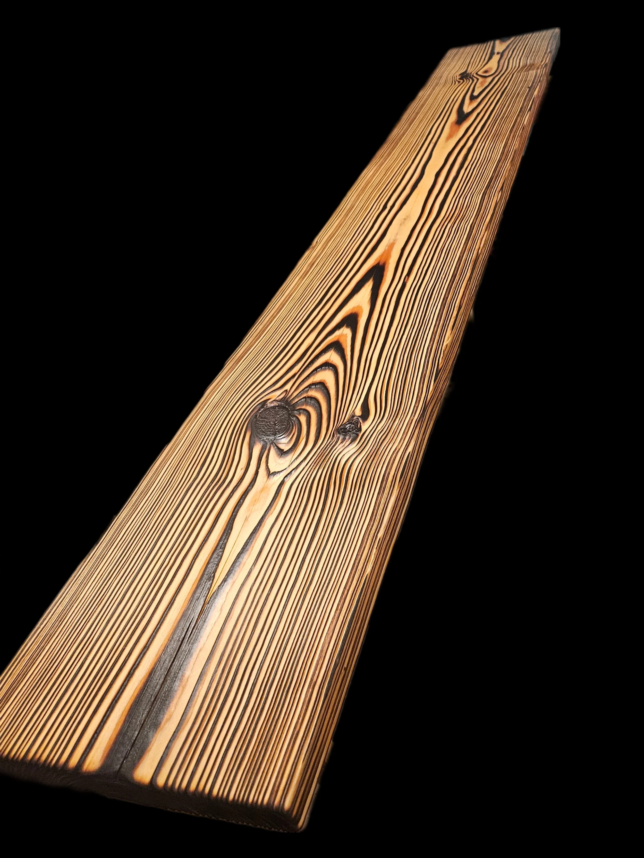 Close-up of a wooden surface with visible grain patterns and knots against a black background.
