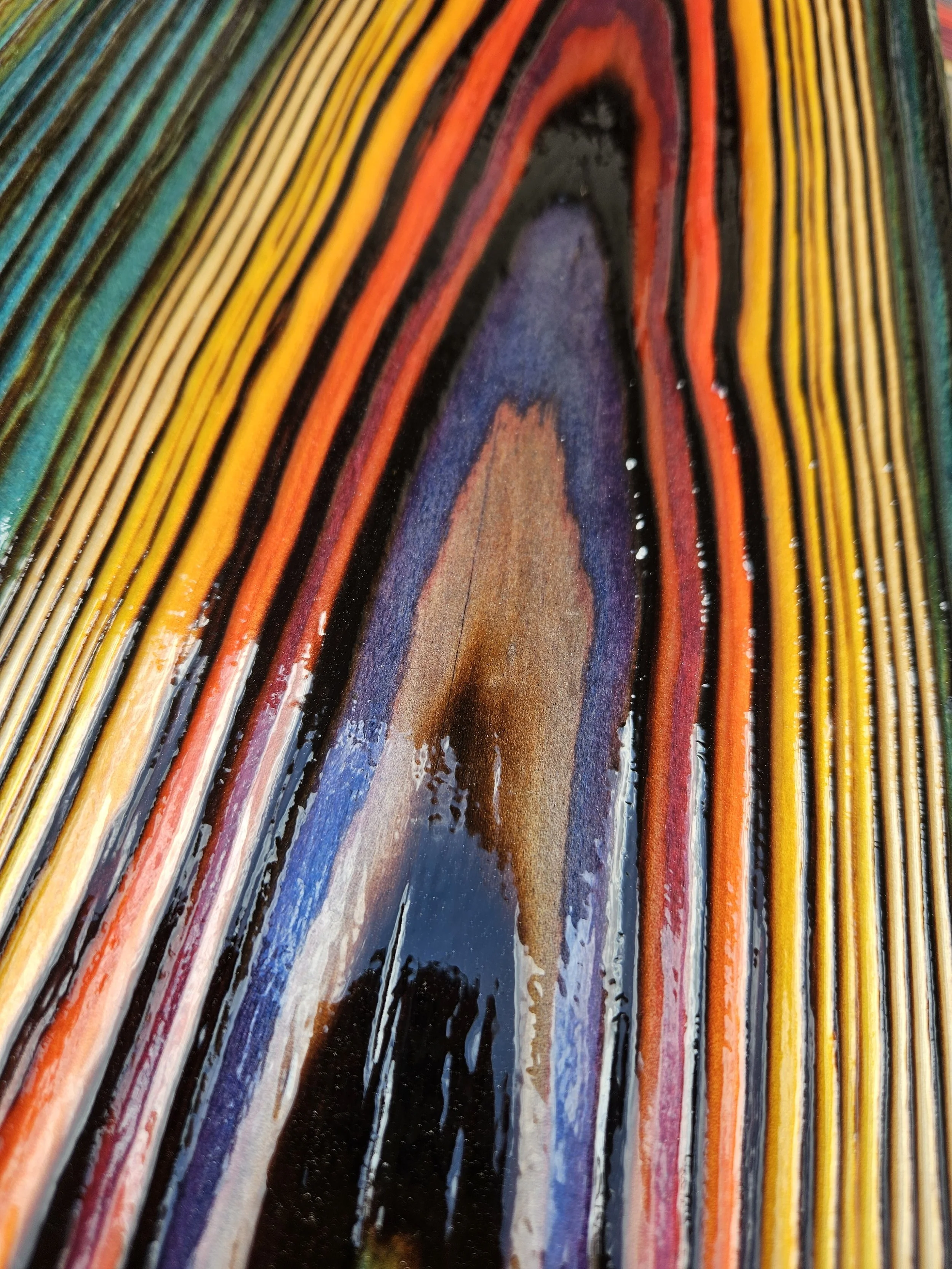 Close-up of colorful layered rocks with black, red, orange, yellow, green, blue, purple, brown, and white hues, showing the mineral banding and texture.