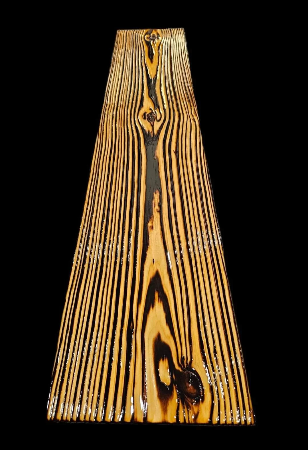 A close-up of a wooden plank with a dark central streak and burn marks, set against a black background.