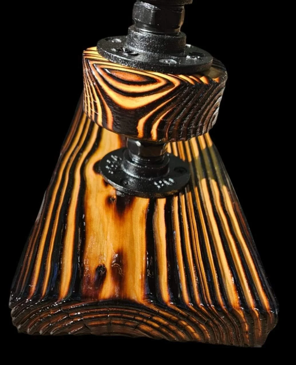 Close-up photo of a wooden lampshade with black and orange wood grain patterns, mounted on a black metal fixture against a black background.