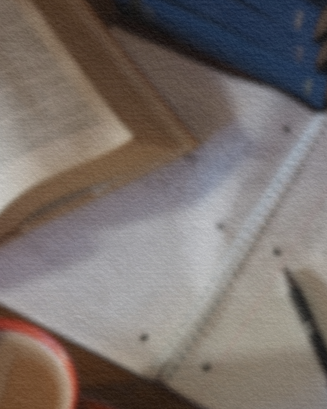 A blurred image of a wooden table or desk with a cup of coffee, a notebook, and some papers on it.
