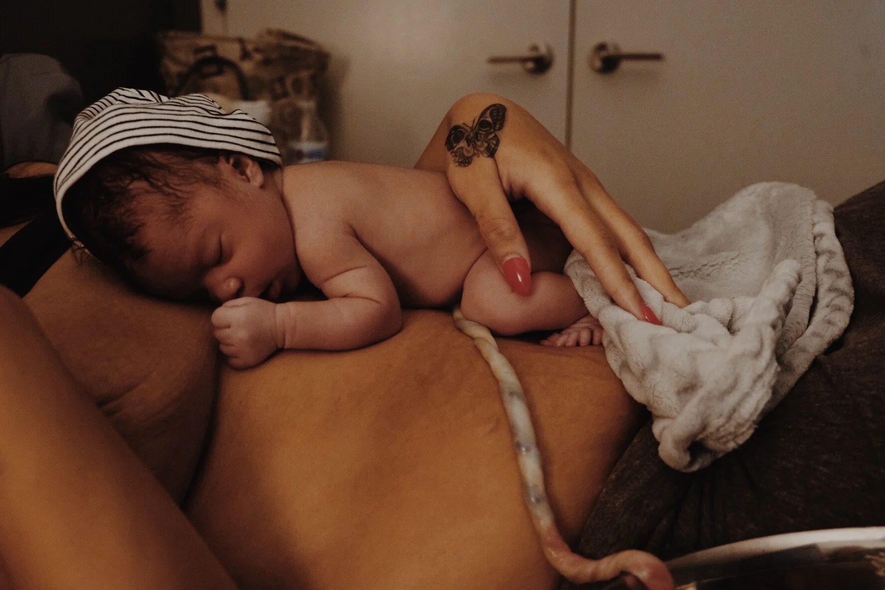 A baby sleeping on a mothers chest in a cozy room, with an adult's hand gently touching the baby's back after a peaceful homebirth