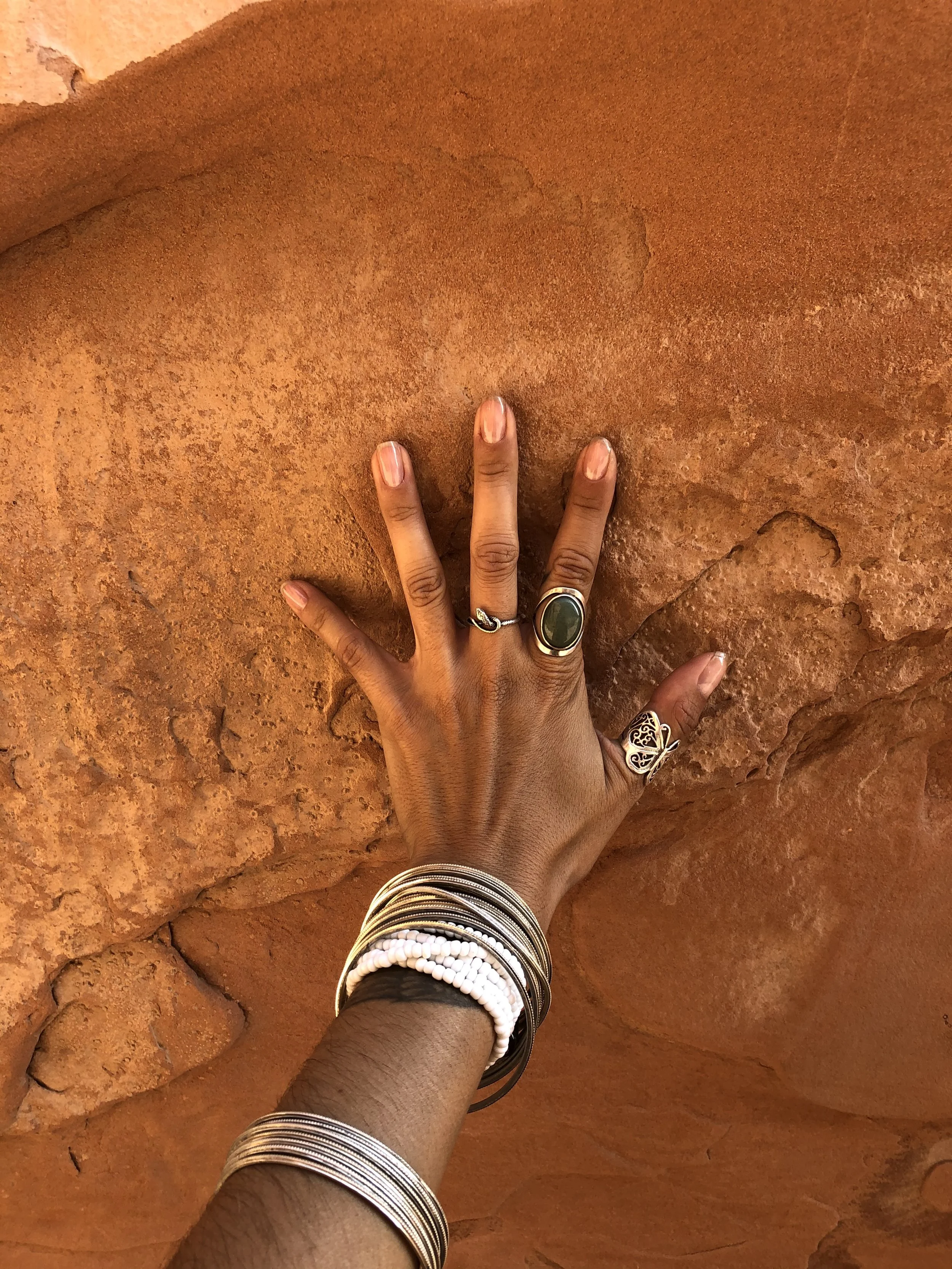 Close-up of a person's hand with rings and bracelets on a textured orange-brown stone surface representing Reiki energy healing for prenatal and postpartum birthing people.