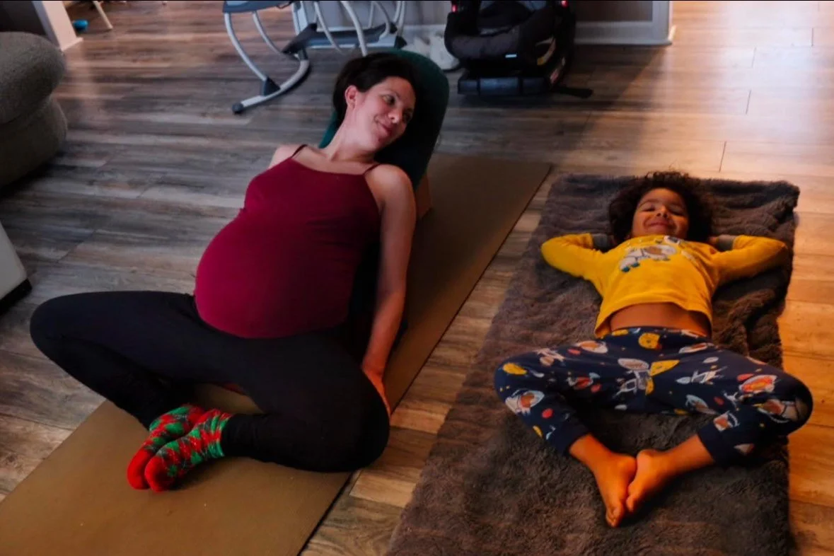 A pregnant woman and hers son lying on yoga mats on a wooden floor, enjoying the prenatal yoga session. These are apart of prenatal sessions that can be incorporated with doula support package