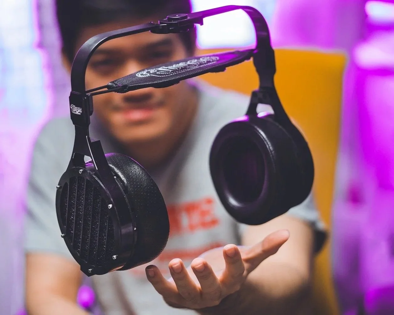 A person is holding a pair of black headphones with a flexible headband and cushioned ear cups, suspended in midair while looking at them.