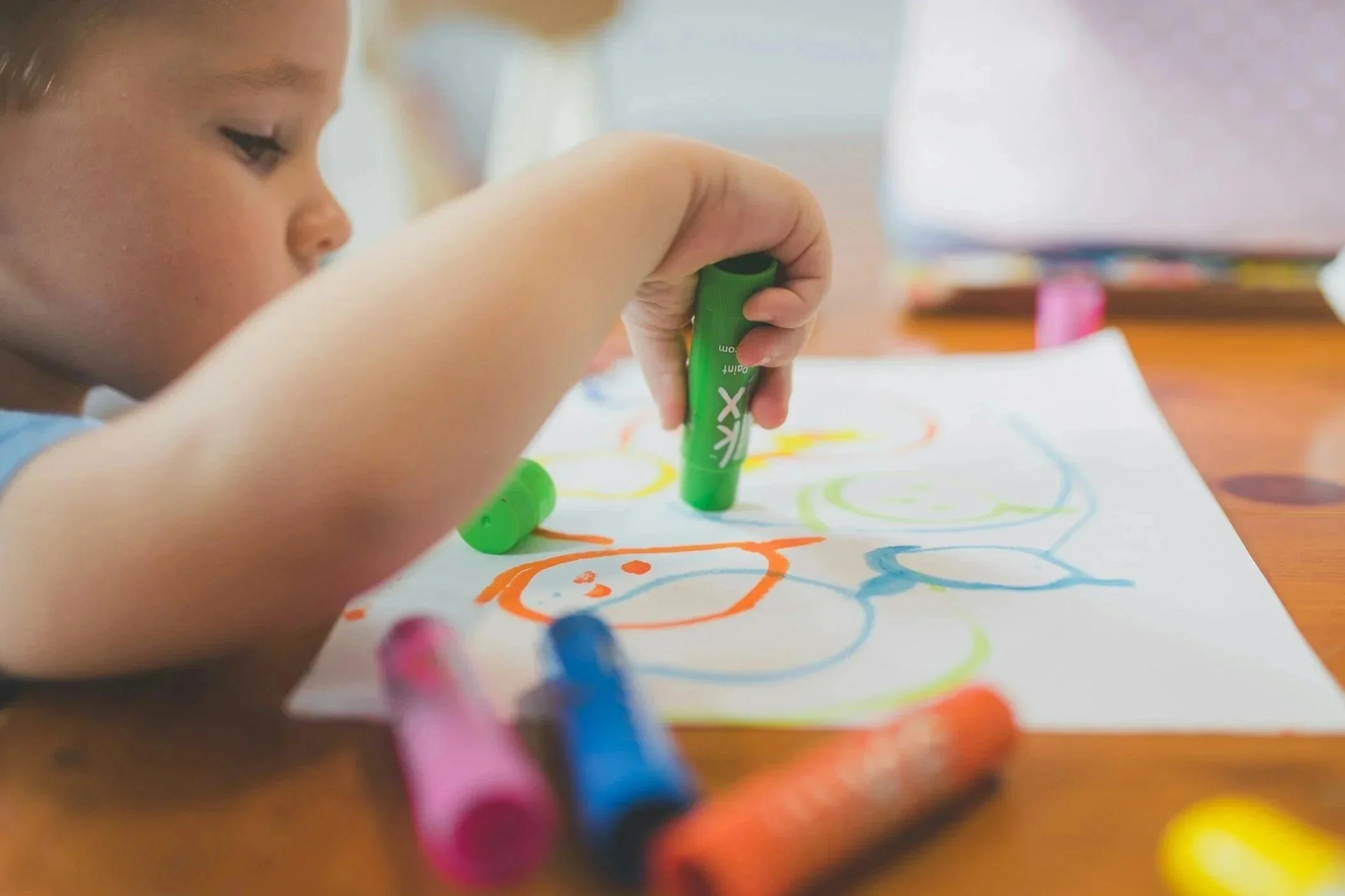 A young child creates a colorful drawing using large markers.