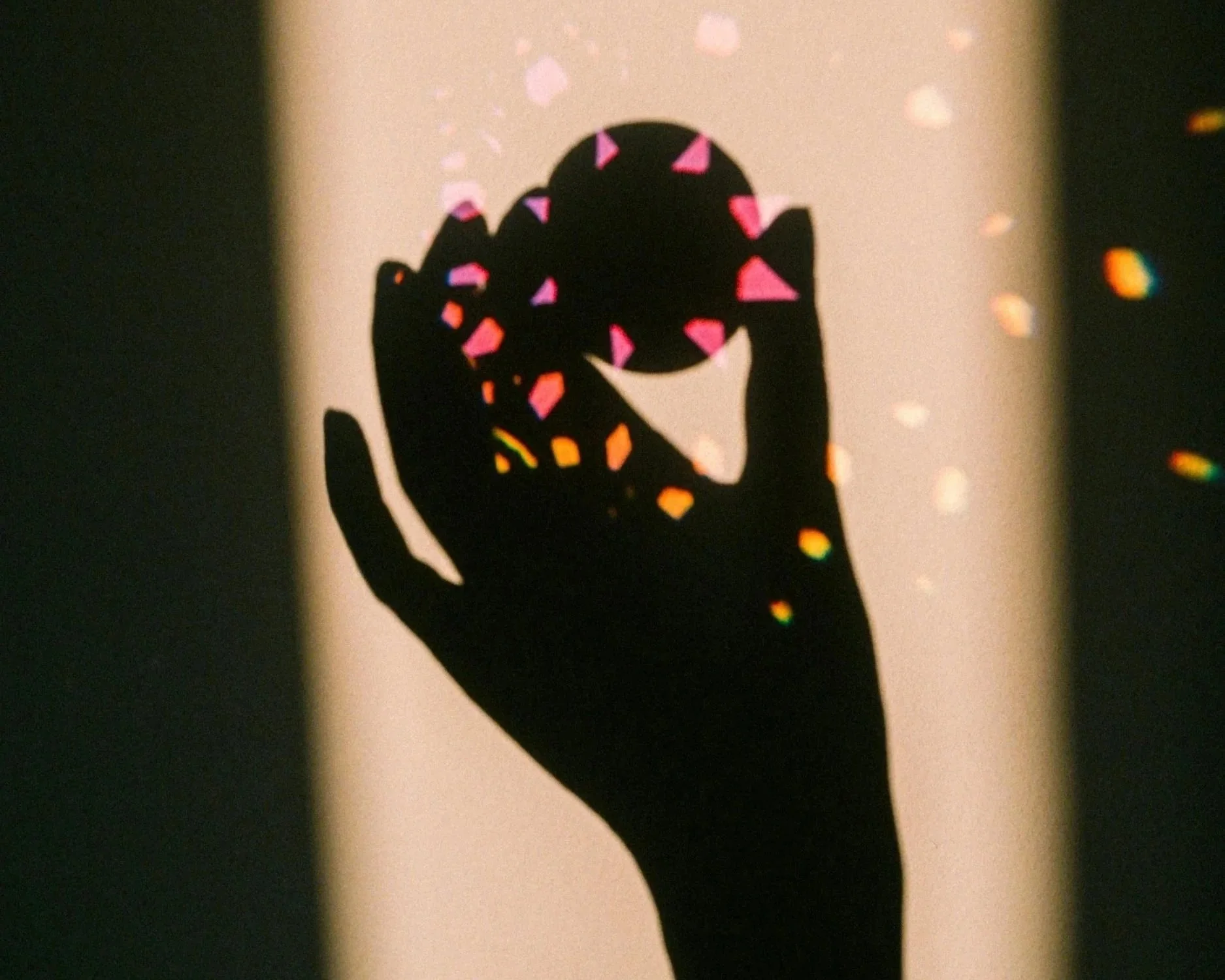 Silhouette of a hand holding a circular object, with colorful light reflections creating a pattern on the object and surrounding area.