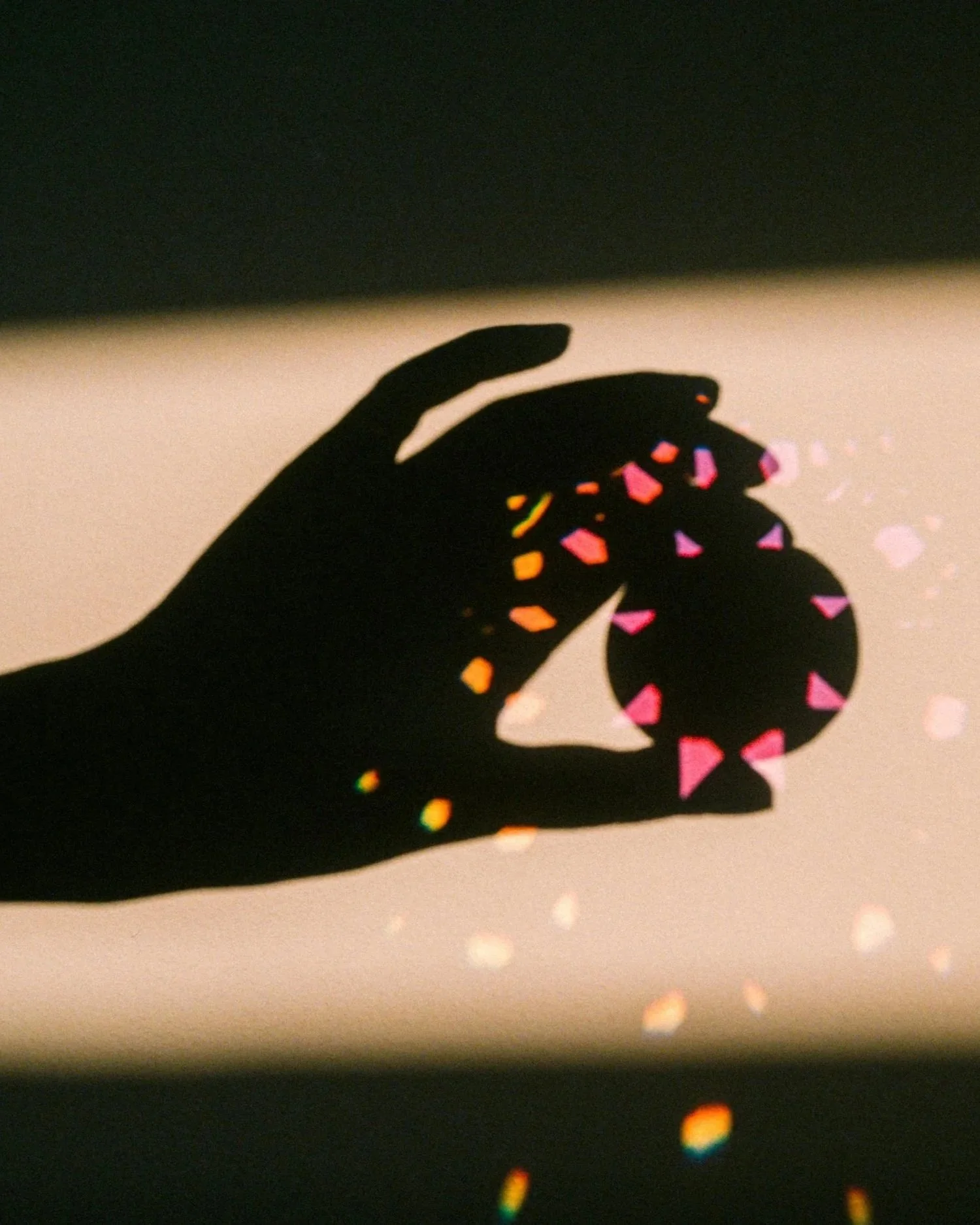 Silhouette of a hand holding a small round object, with colorful light reflections creating rainbow-like patterns on the hand and object.
