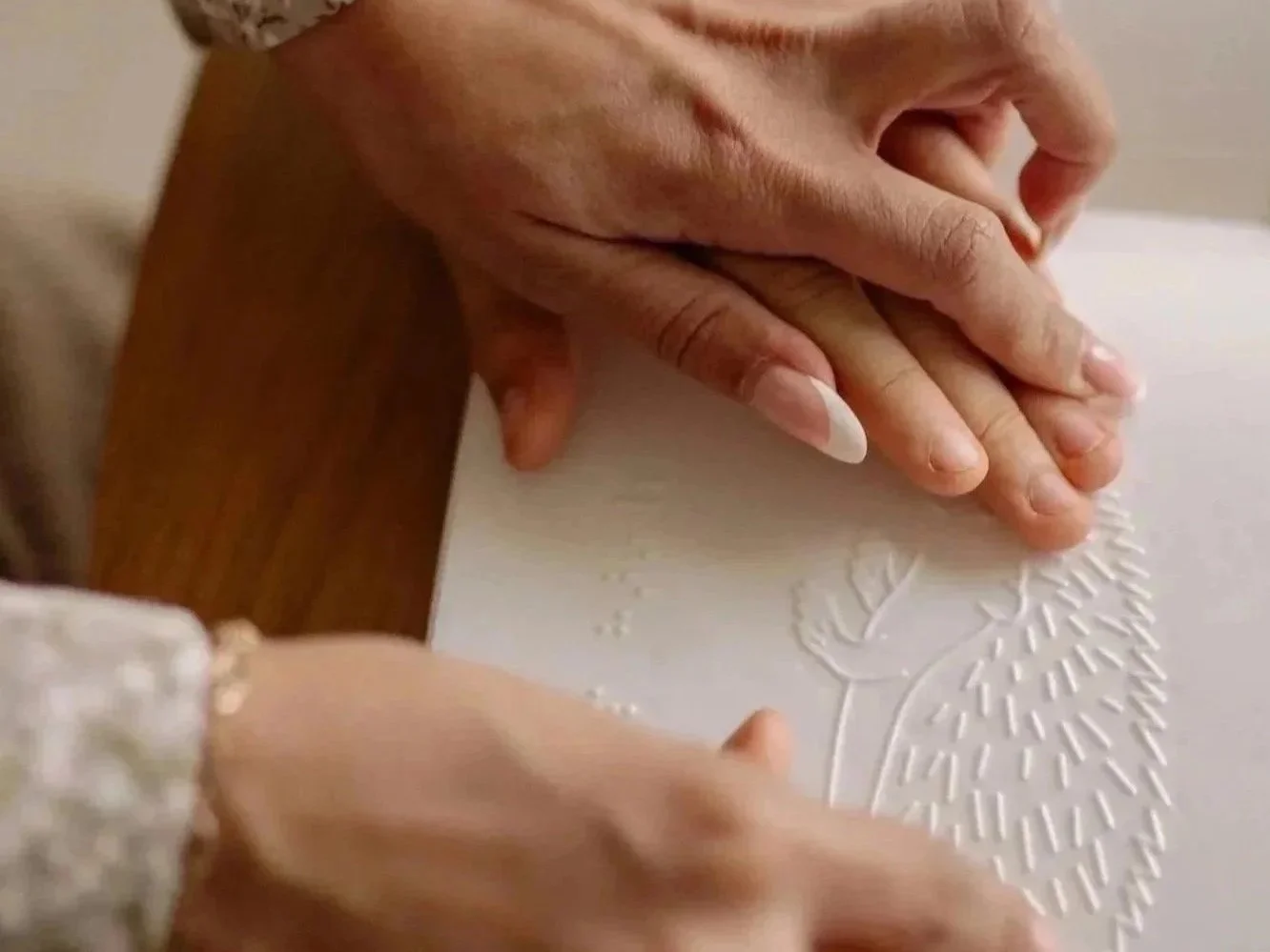 Two hands, one adult and one child, touching a white surface with an embossed hedgehog.