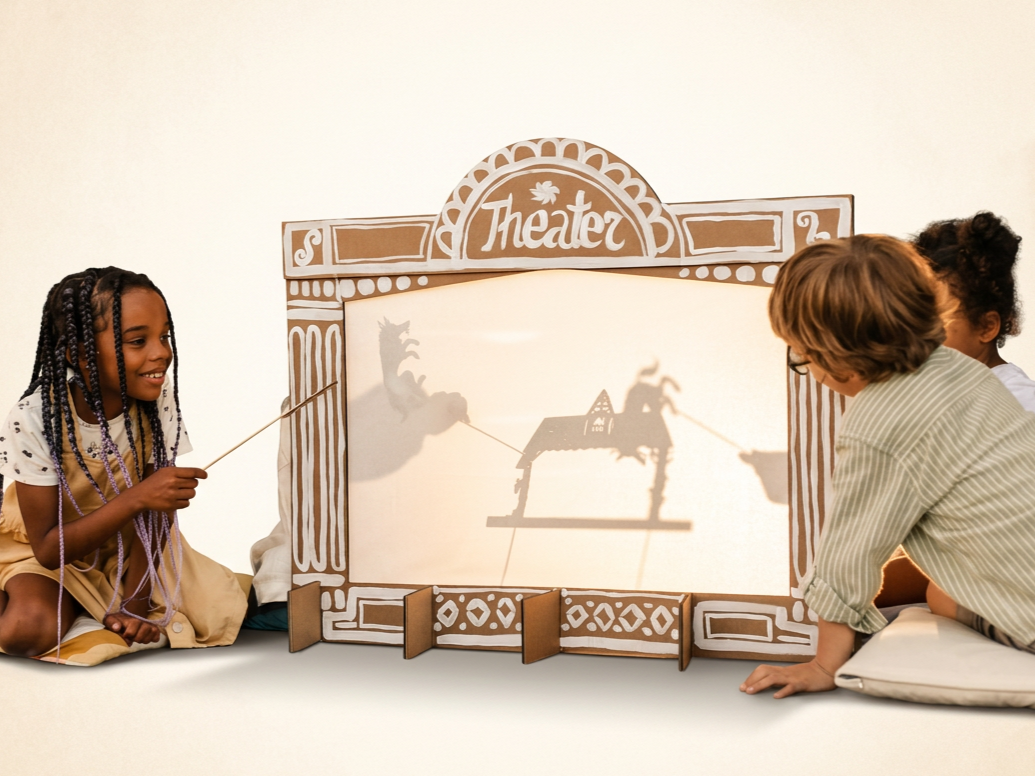 Children play with homemade paper puppets on sticks behind a screen with light shining behind it to create a shadow puppet show.