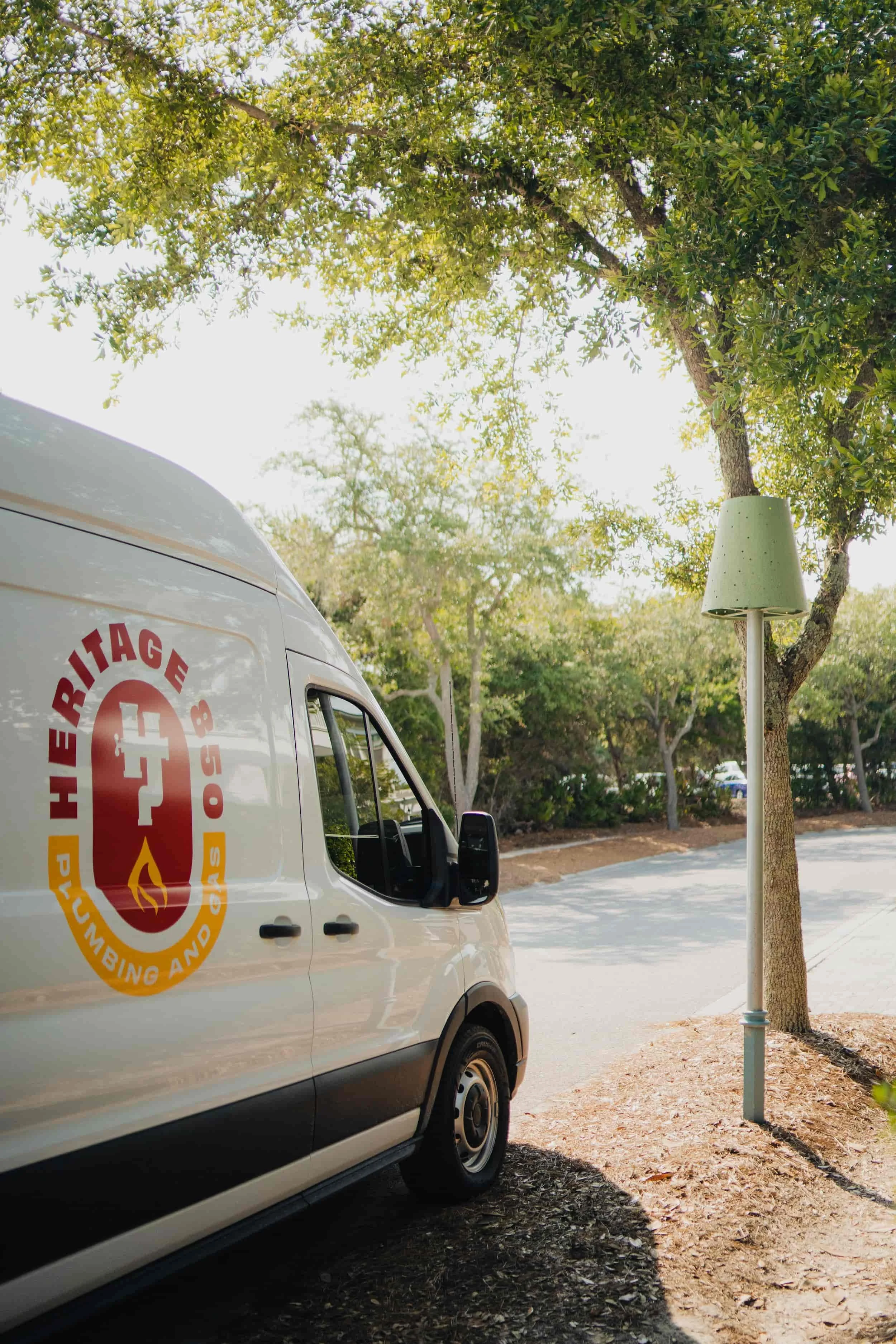 Photo of a white emergency services van parked on a shaded street under trees, with a lamp post nearby.