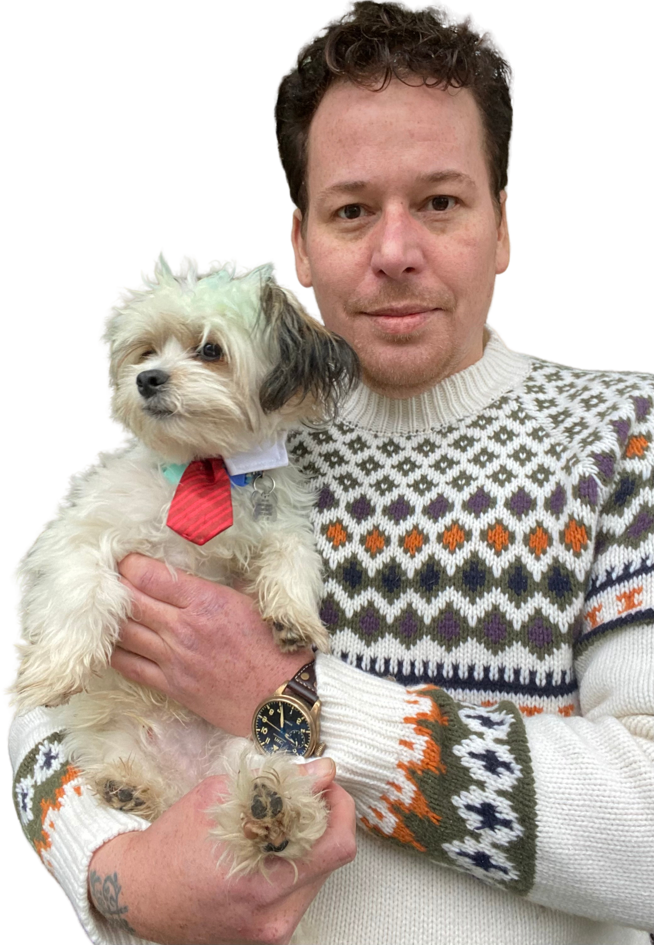 A man holding a small, fluffy dog with a red tie. The man is wearing a colorful patterned sweater and a watch. The background is plain and dark.