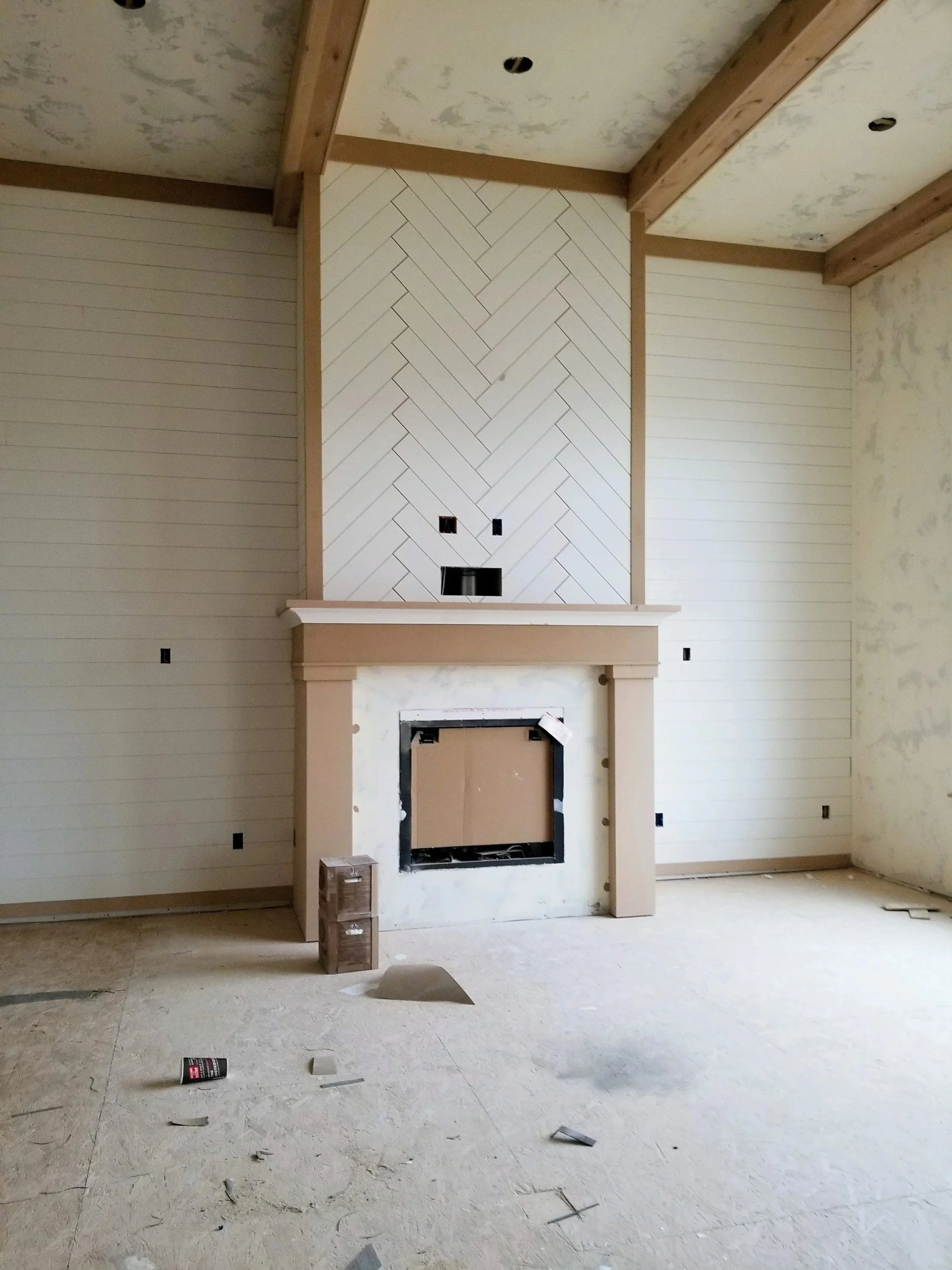 Custom fireplace feature wall with a herringbone wood accent, shiplap panels, exposed ceiling beams, and a handcrafted mantel installed by CBR Interiors in a Utah home.