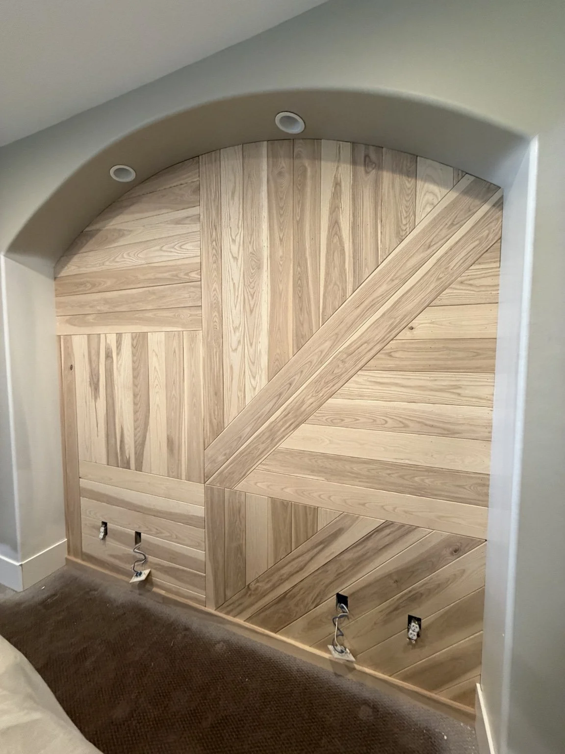 Custom geometric wood accent wall installed inside an arched niche by CBR Interiors in a Salt Lake City, Utah home. The design combines vertical, horizontal, and diagonal hardwood planks to create a one-of-a-kind architectural feature wall.